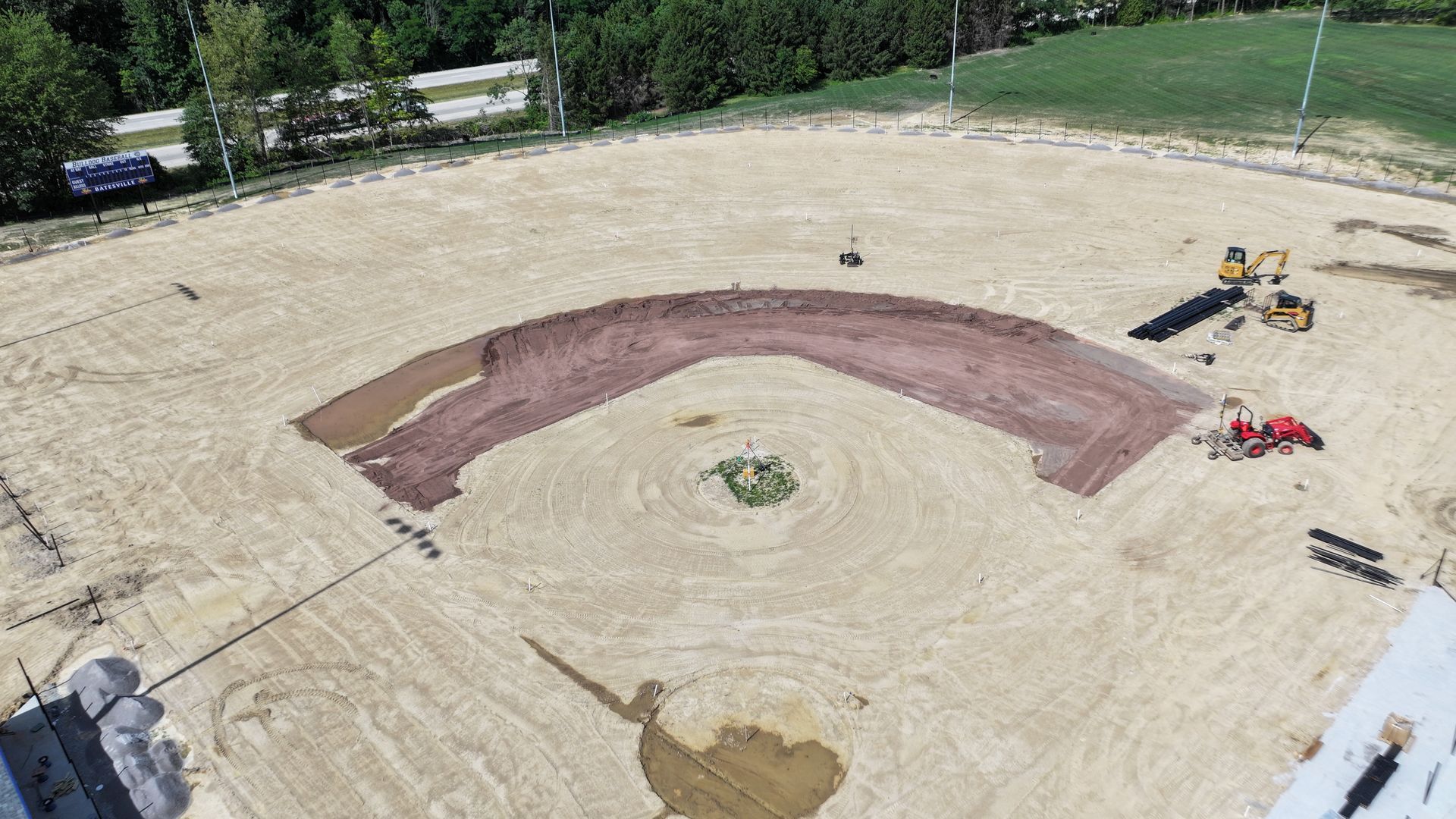 Aerial view of a sand volleyball court under construction with a curved dark surface and equipment nearby