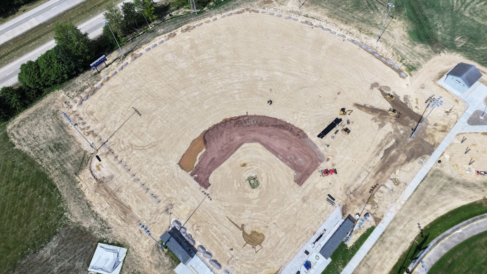 Aerial view of a sandy baseball field with a red-brown infield and surrounding walkways.