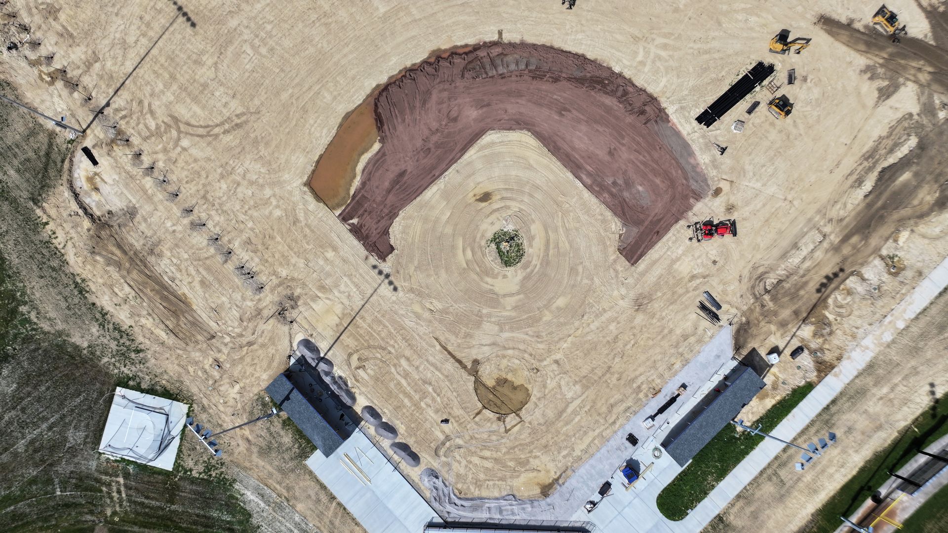 Aerial view of a construction site with a curved concrete foundation, equipment, and surrounding dirt lot.