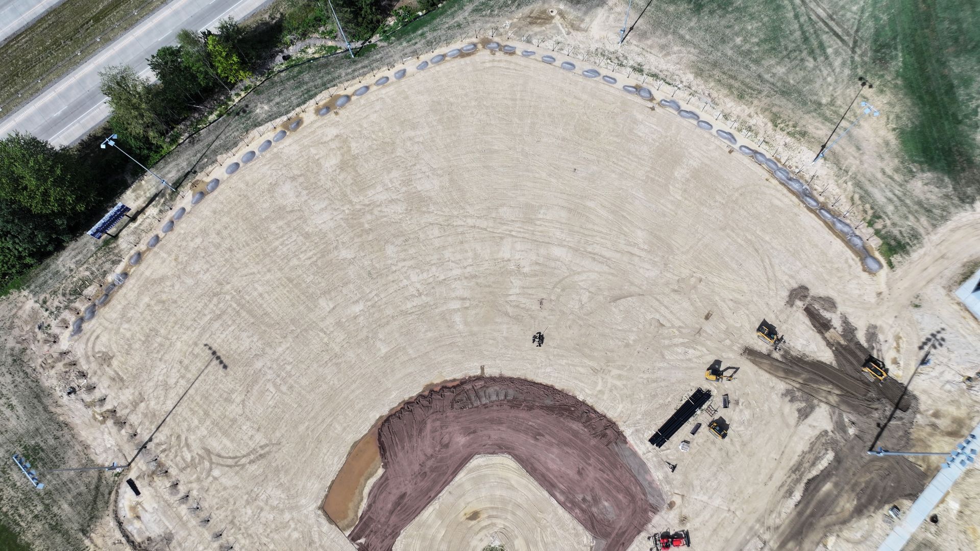 Aerial view of a curved dirt baseball field with a pitcher’s mound and surrounding trees.