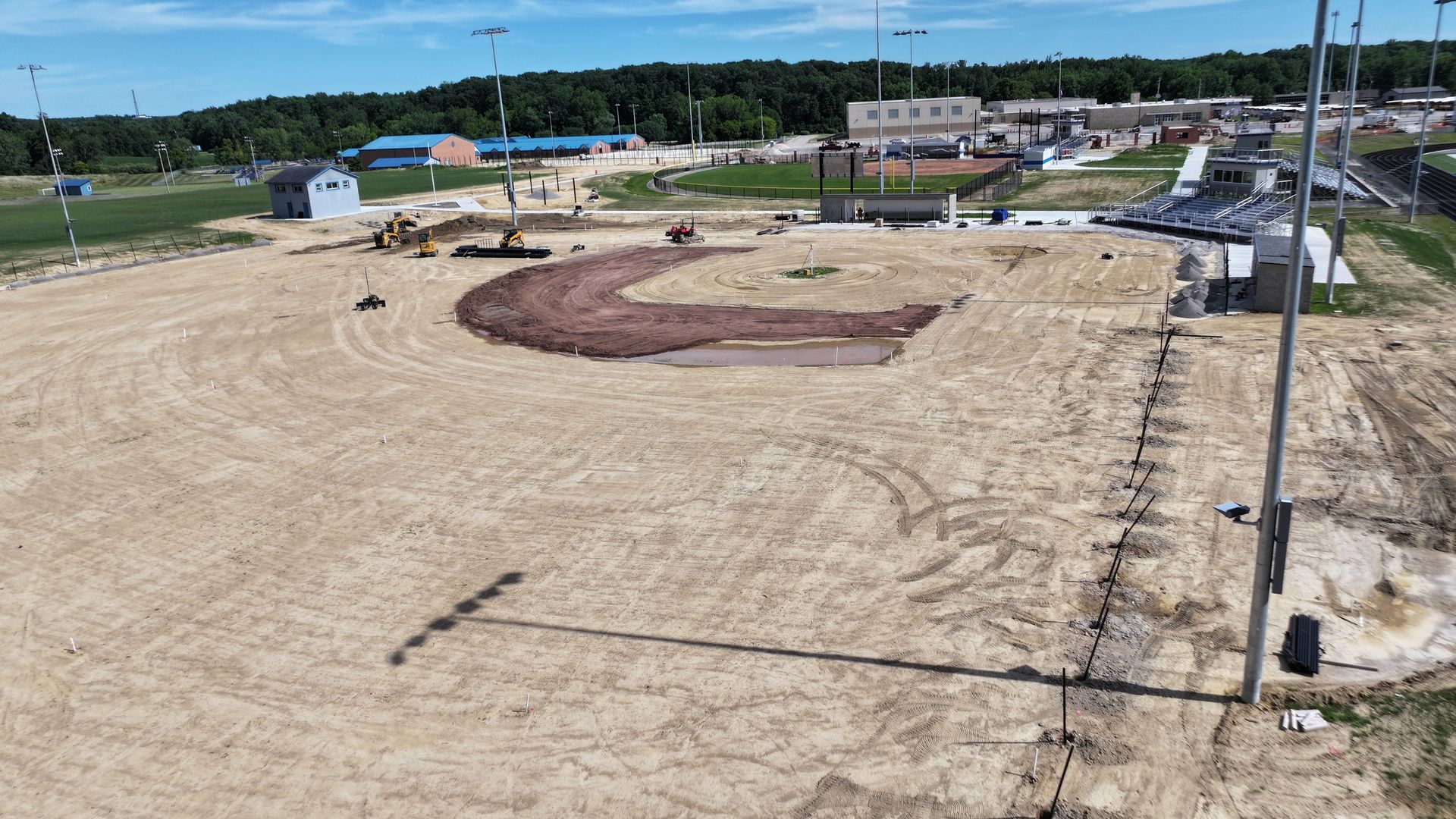 Dirt construction site with curved landscaped beds and gravel paths near houses and utility poles