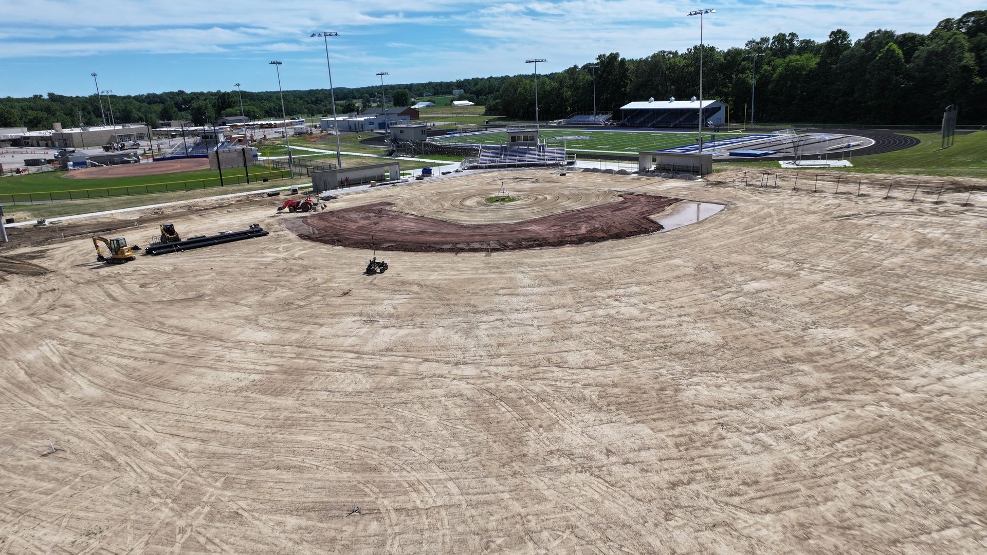 Construction site with a large sandy area, dirt mound, and scattered equipment under a clear sky