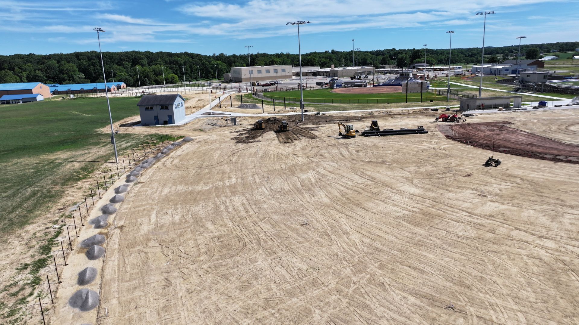 Construction site with cleared dirt field, equipment, and a small utility building under a blue sky
