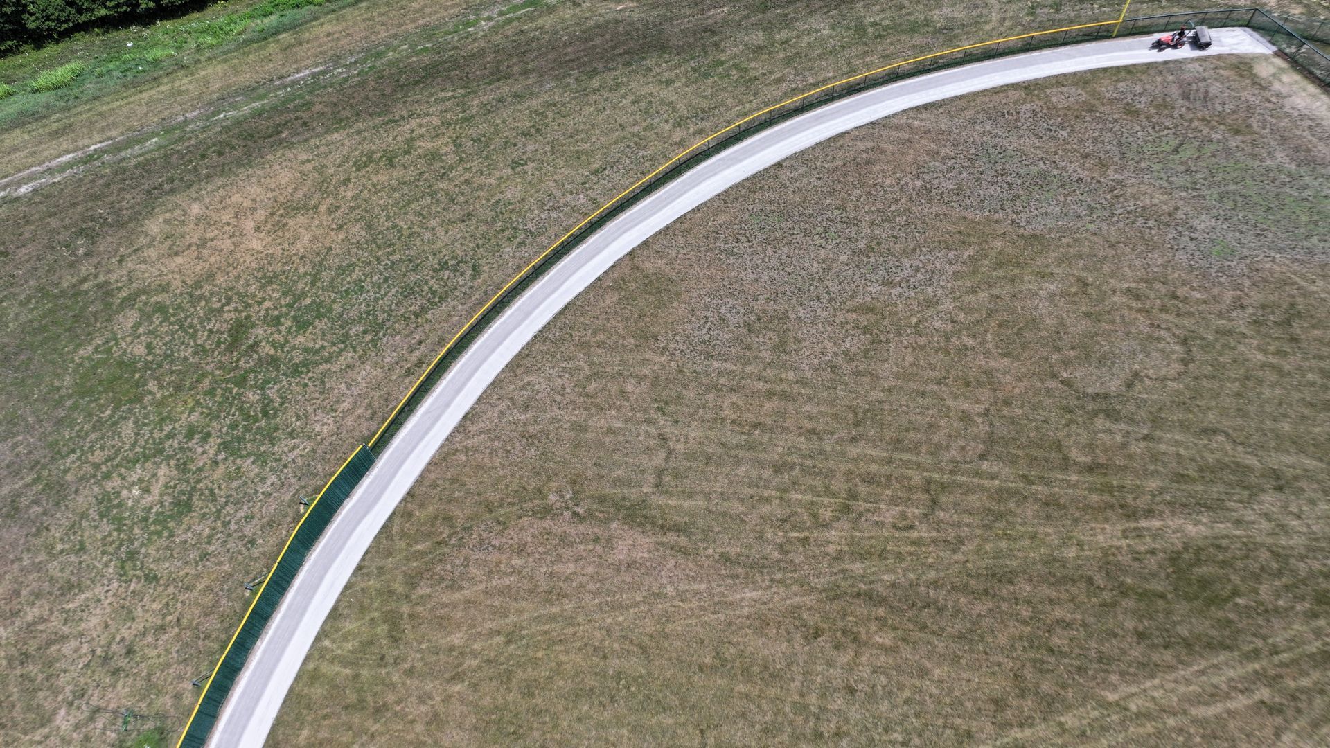 Curved white path through a grassy field with a small vehicle near the top edge