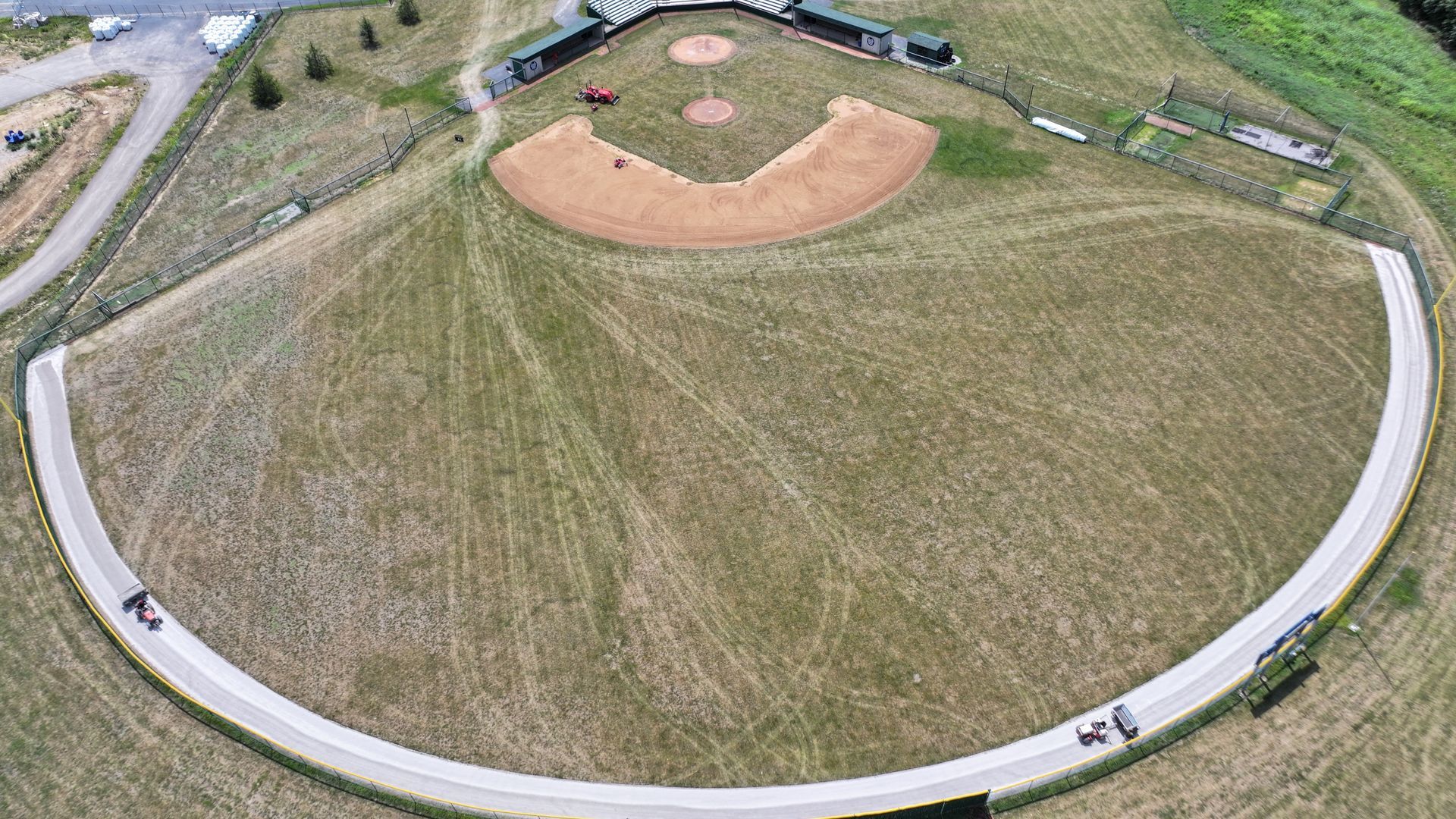 Aerial view of a baseball field surrounded by a white oval track and grassy open space.