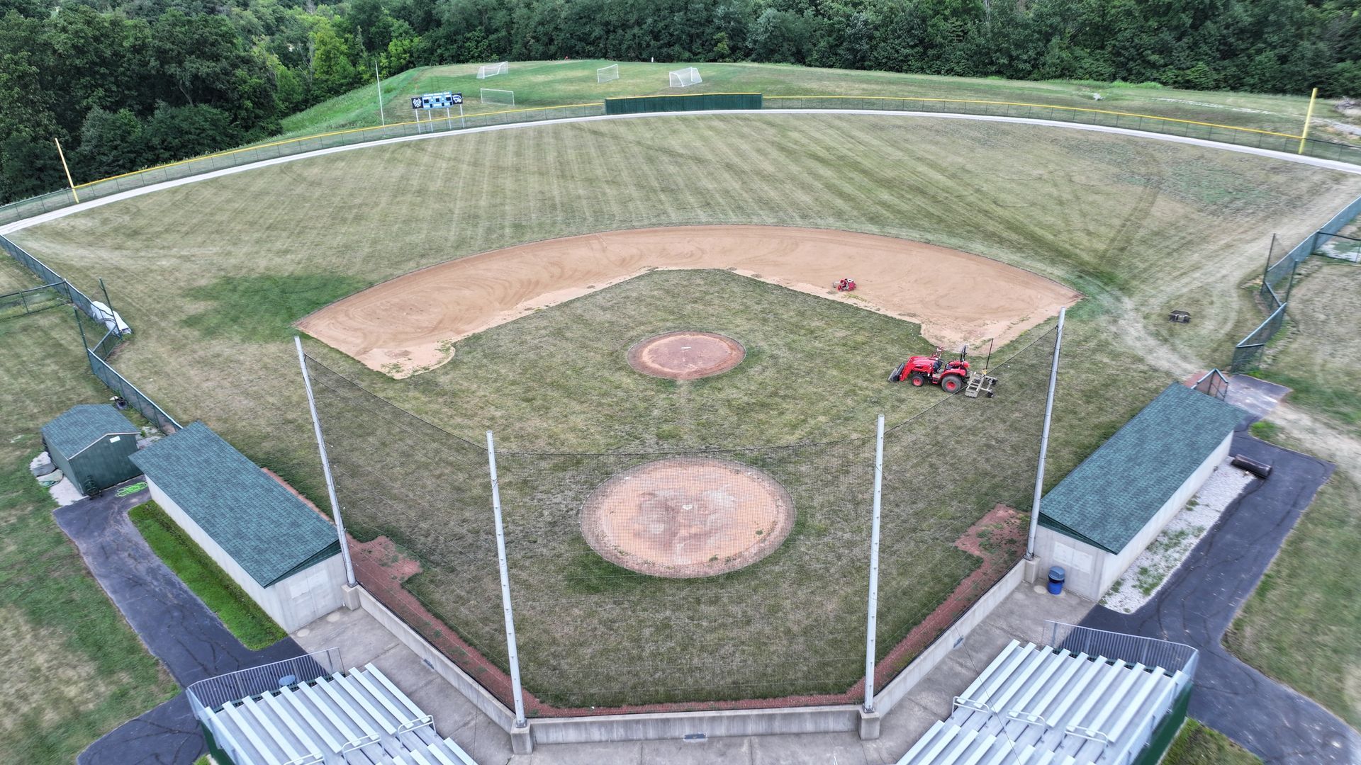 Aerial view of a baseball field with a dirt infield, green outfield, and empty bleachers.