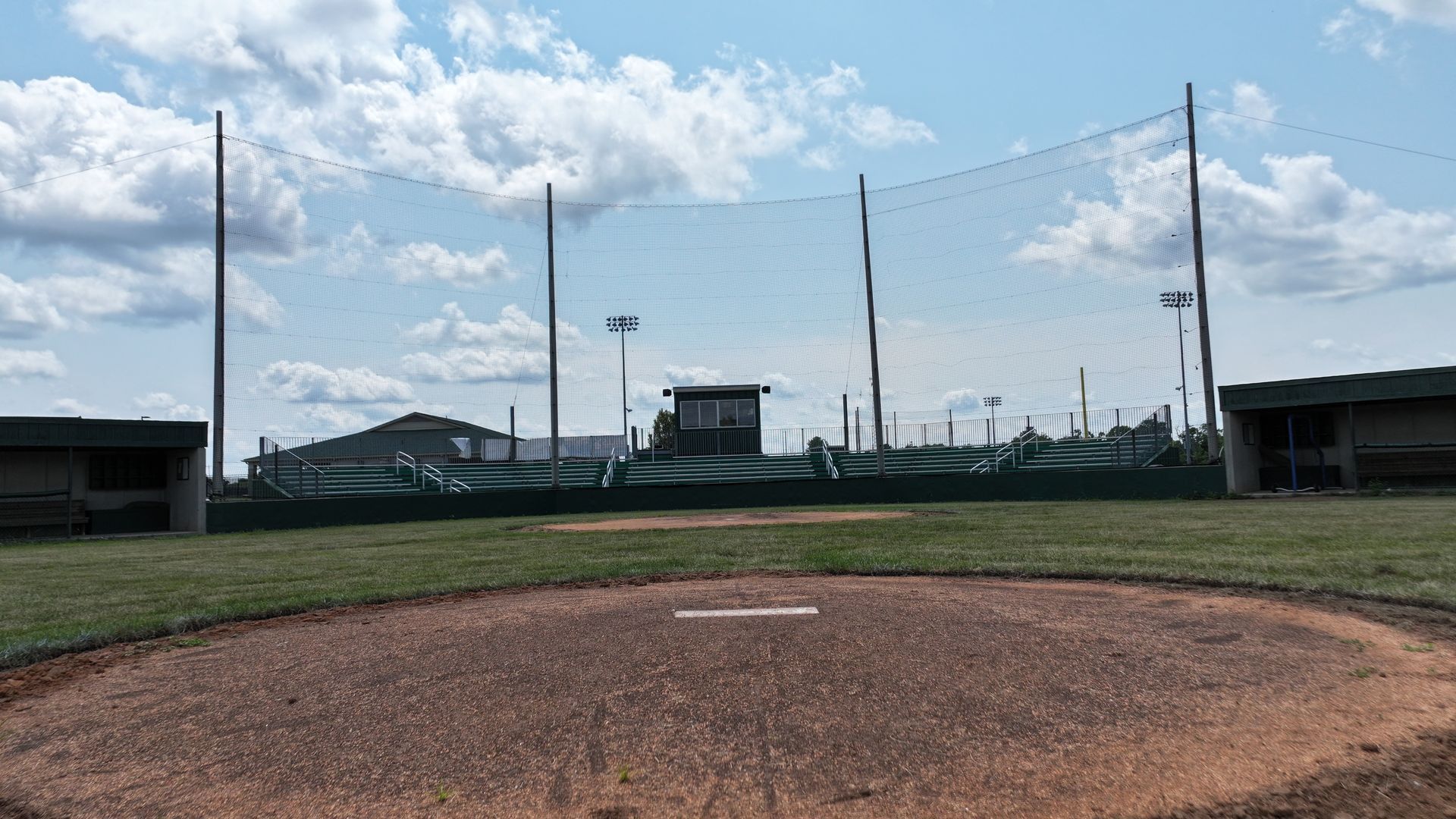 Empty baseball field under a blue sky with clouds and tall light poles