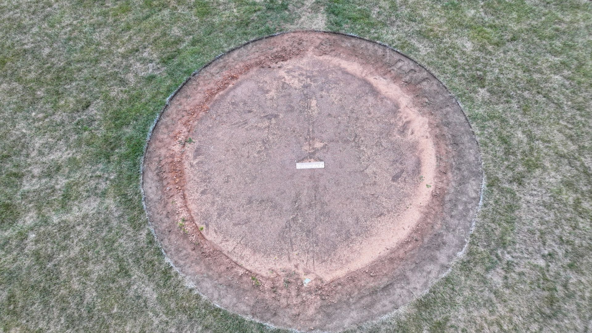 Circular concrete or stone marker in grass, with a small white tag at the center.
