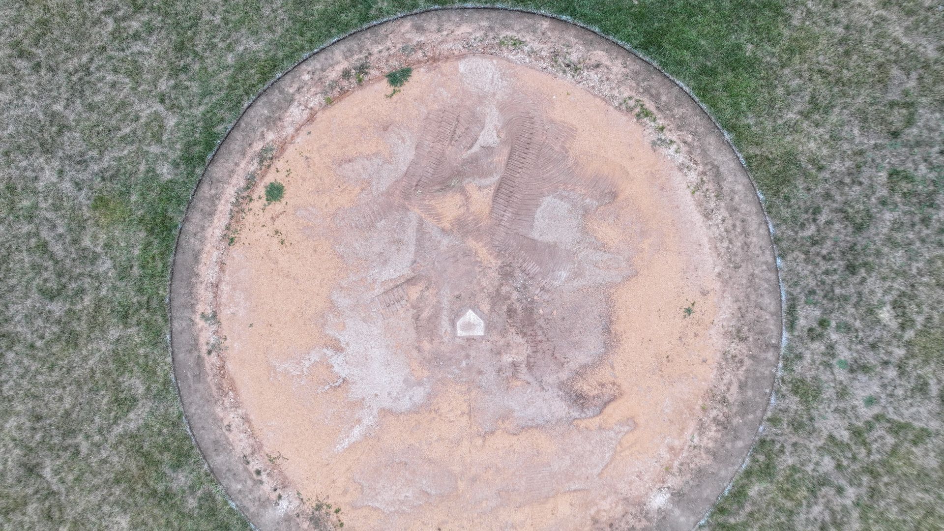 Circular tan patch or concrete pad surrounded by grass, viewed from above.