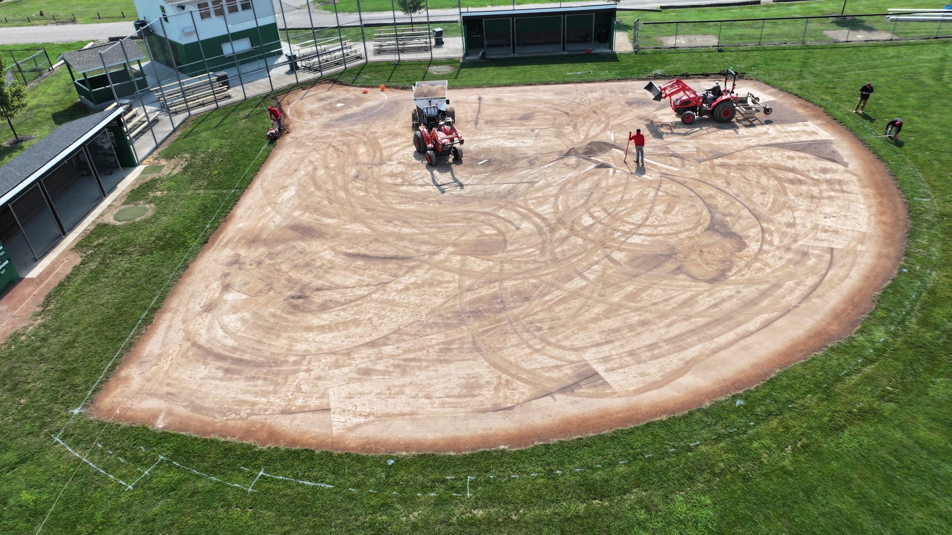 Horse-drawn cart on a dirt oval track with people and equipment nearby, viewed from above