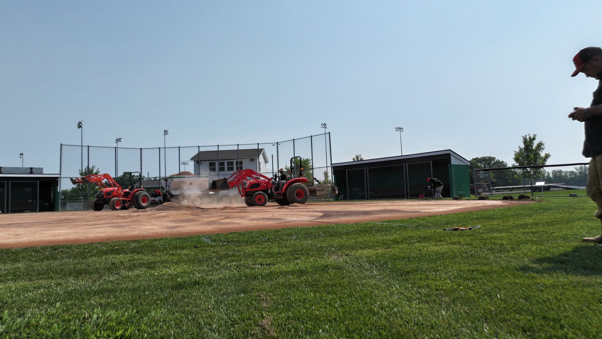 Red tractors lined up on a dirt lot beside a small building and grassy field under a clear sky