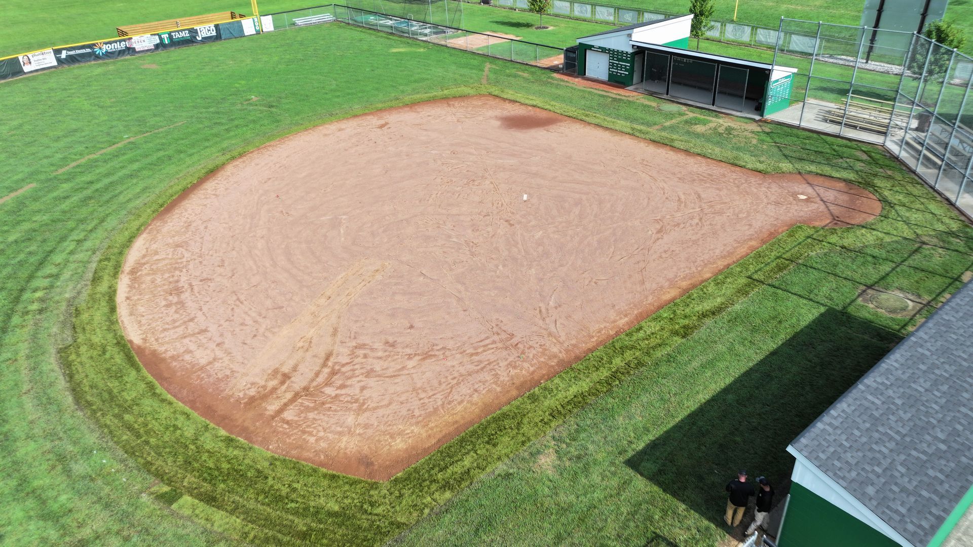 Empty baseball infield with a dirt diamond and green grass, viewed from above.