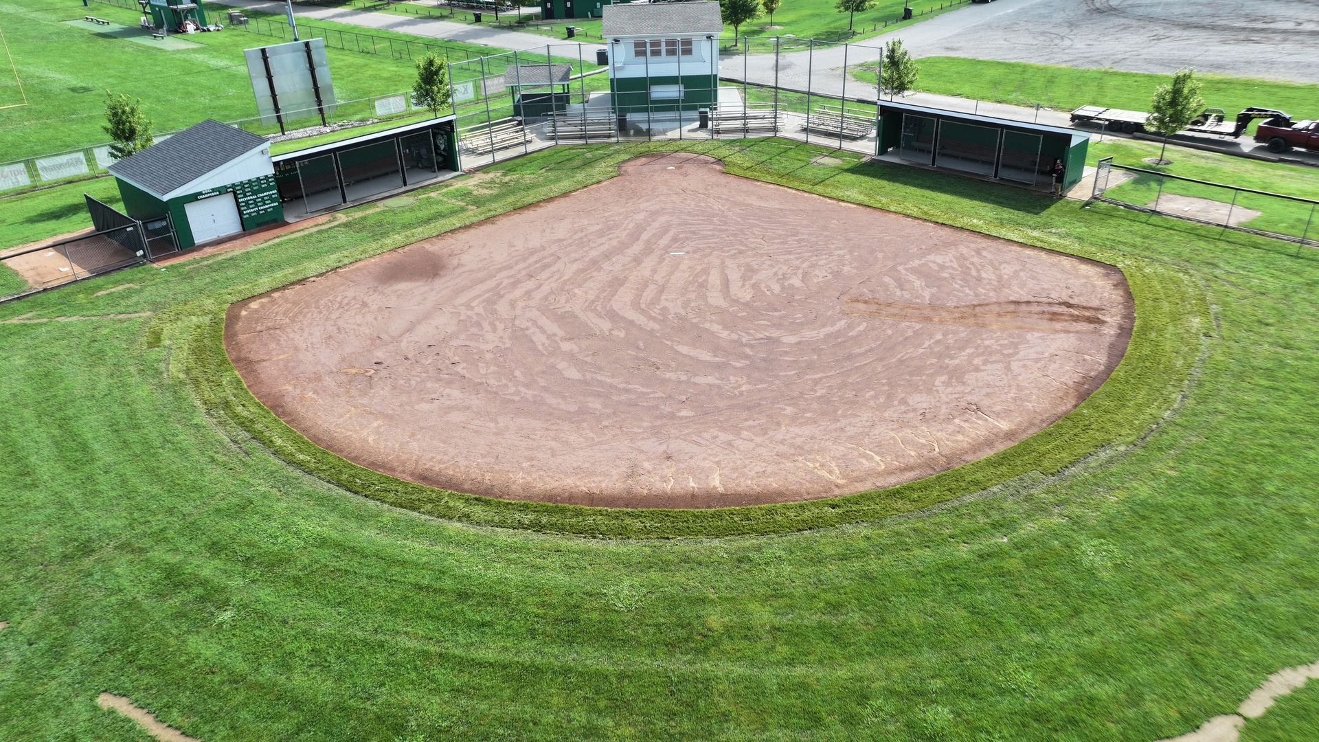 Aerial view of a baseball field with a brown dirt infield and green grass outfield near buildings