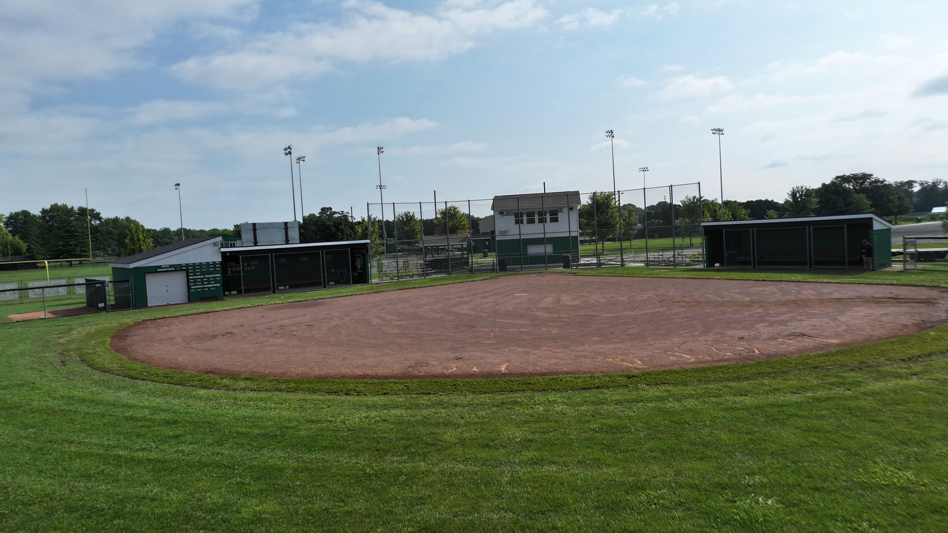 Baseball field with a dirt infield, green grass, and dugouts under a cloudy sky.