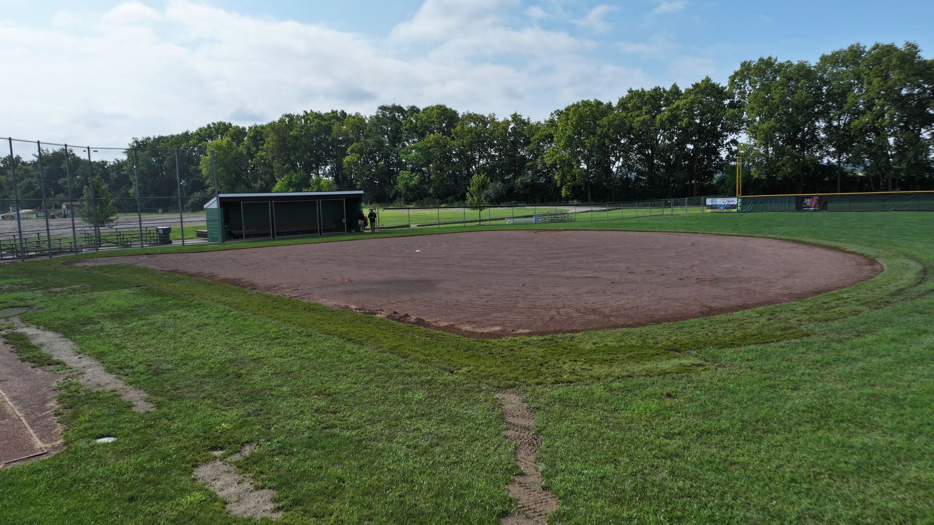 Empty baseball field with a dirt infield, grassy outfield, and trees in the background