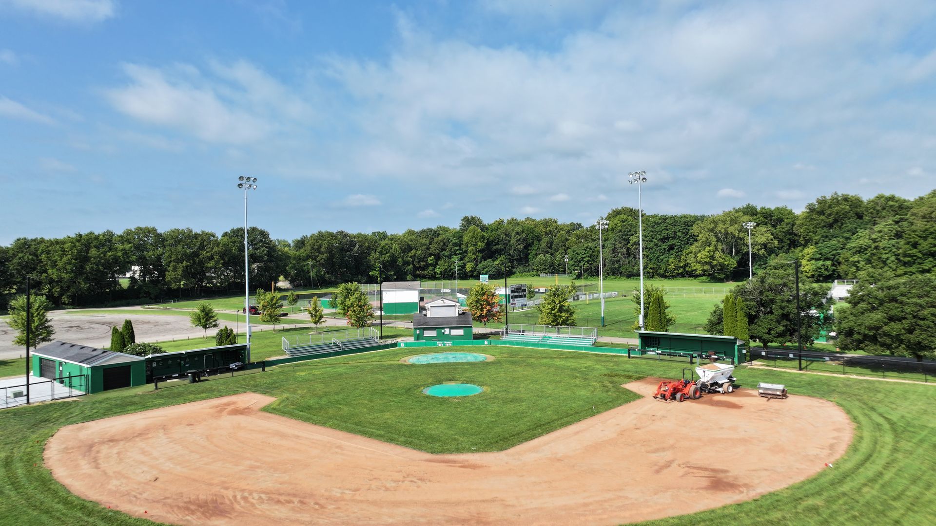 Baseball field with dirt infield, green outfield, scoreboard, and dugouts under a clear sky