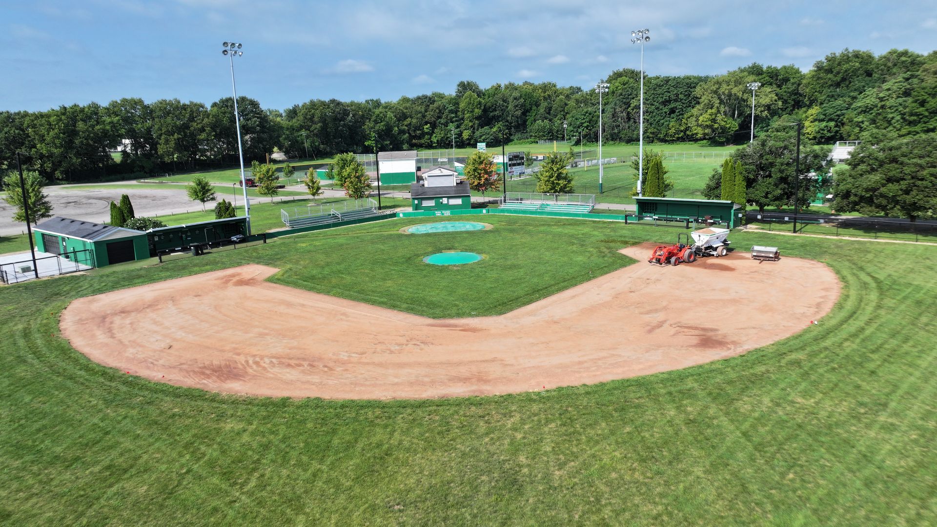 Baseball field under maintenance, with dirt infield, green outfield, and a mower on the right side