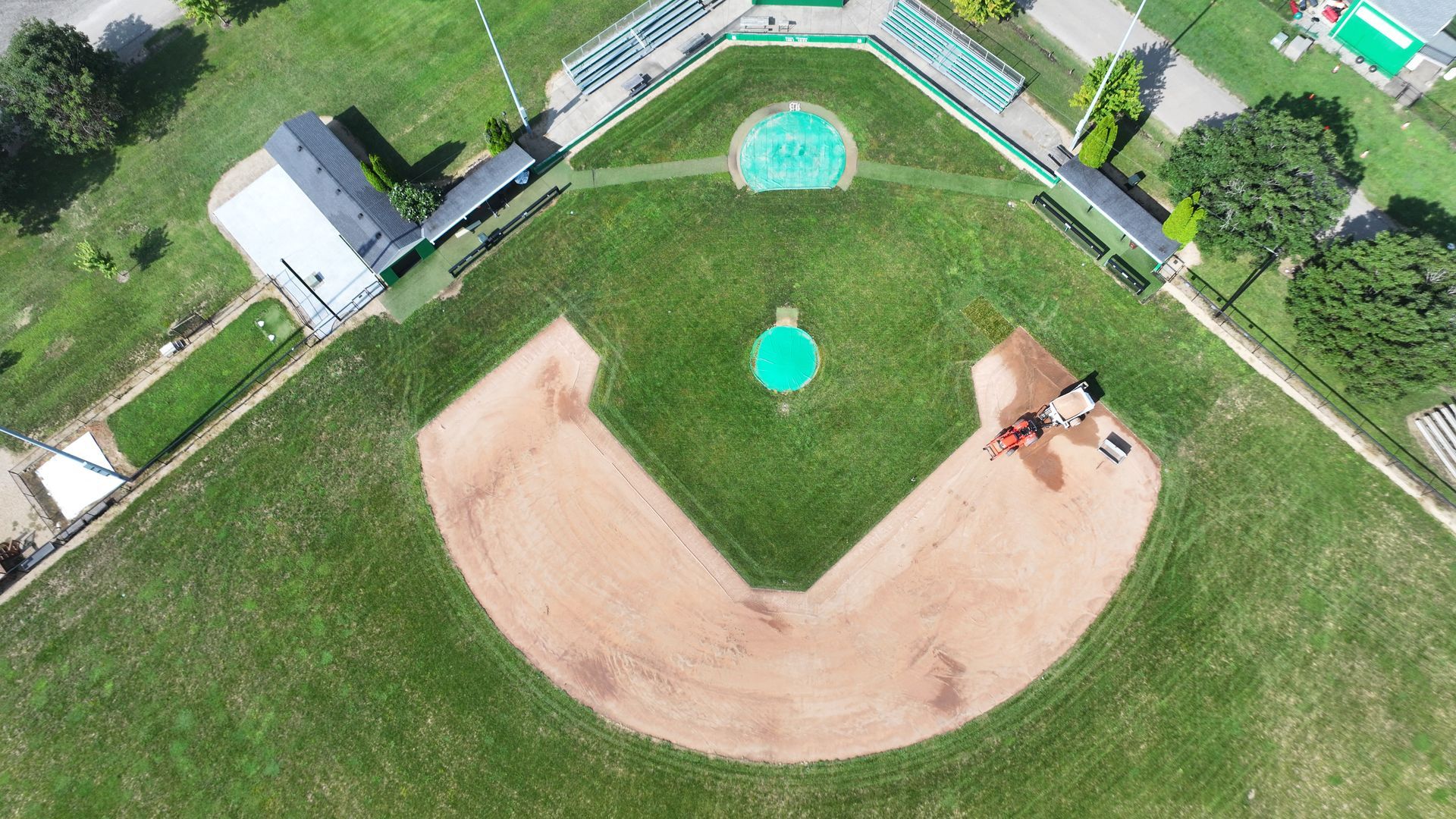 Aerial view of a baseball field with a dirt infield, green outfield, and adjacent buildings.