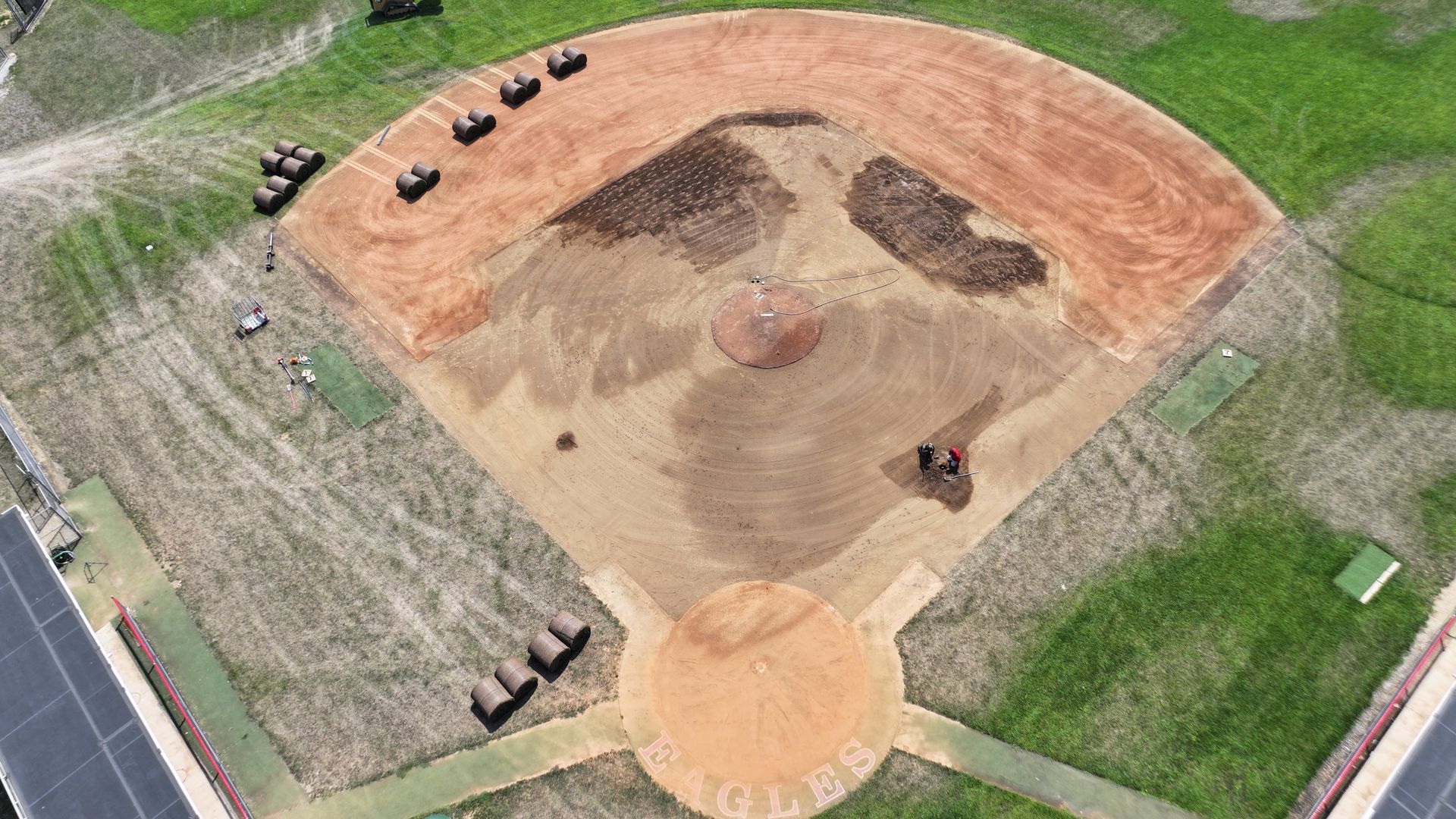 Aerial view of a baseball field with dirt infield, grass outfield, and groundskeeping equipment nearby