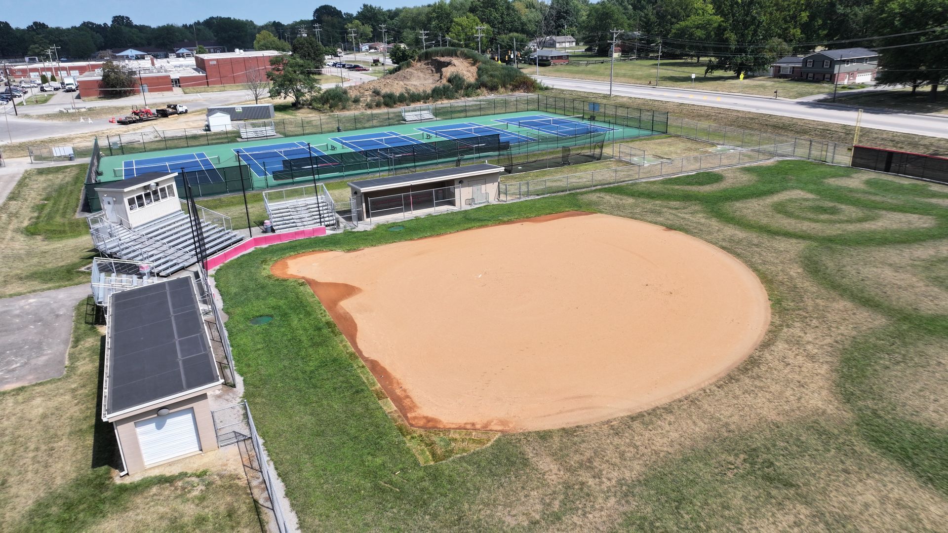 Aerial view of a baseball field with a dirt infield, green outfield, and surrounding buildings