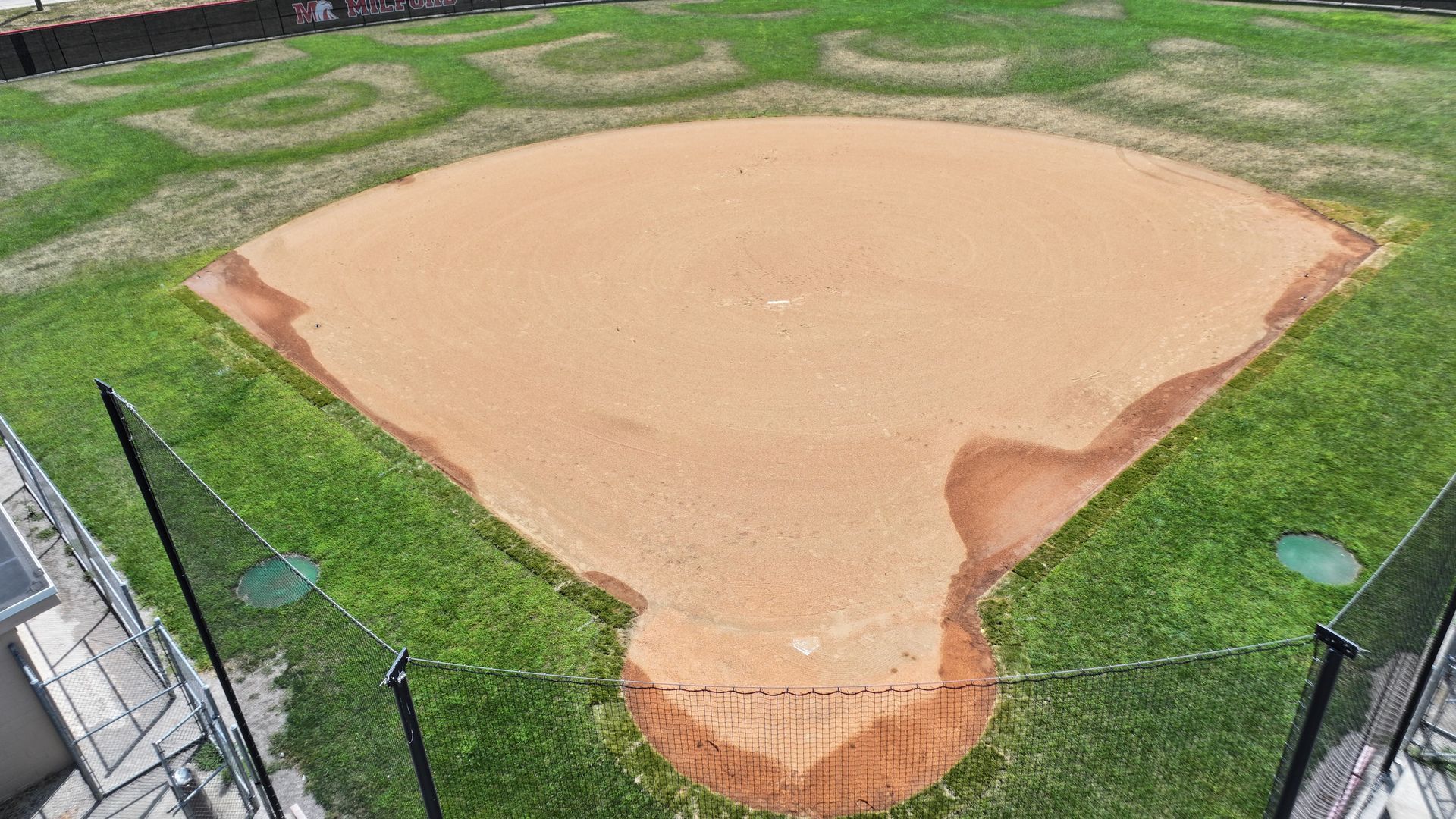 Aerial view of a baseball infield with a tan dirt diamond and green grass outfield.