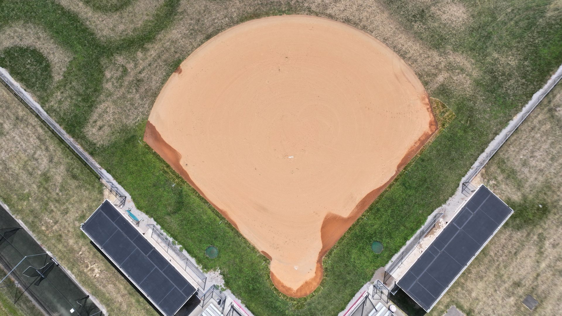 Aerial view of a baseball field with a tan dirt infield and green grass outfield.