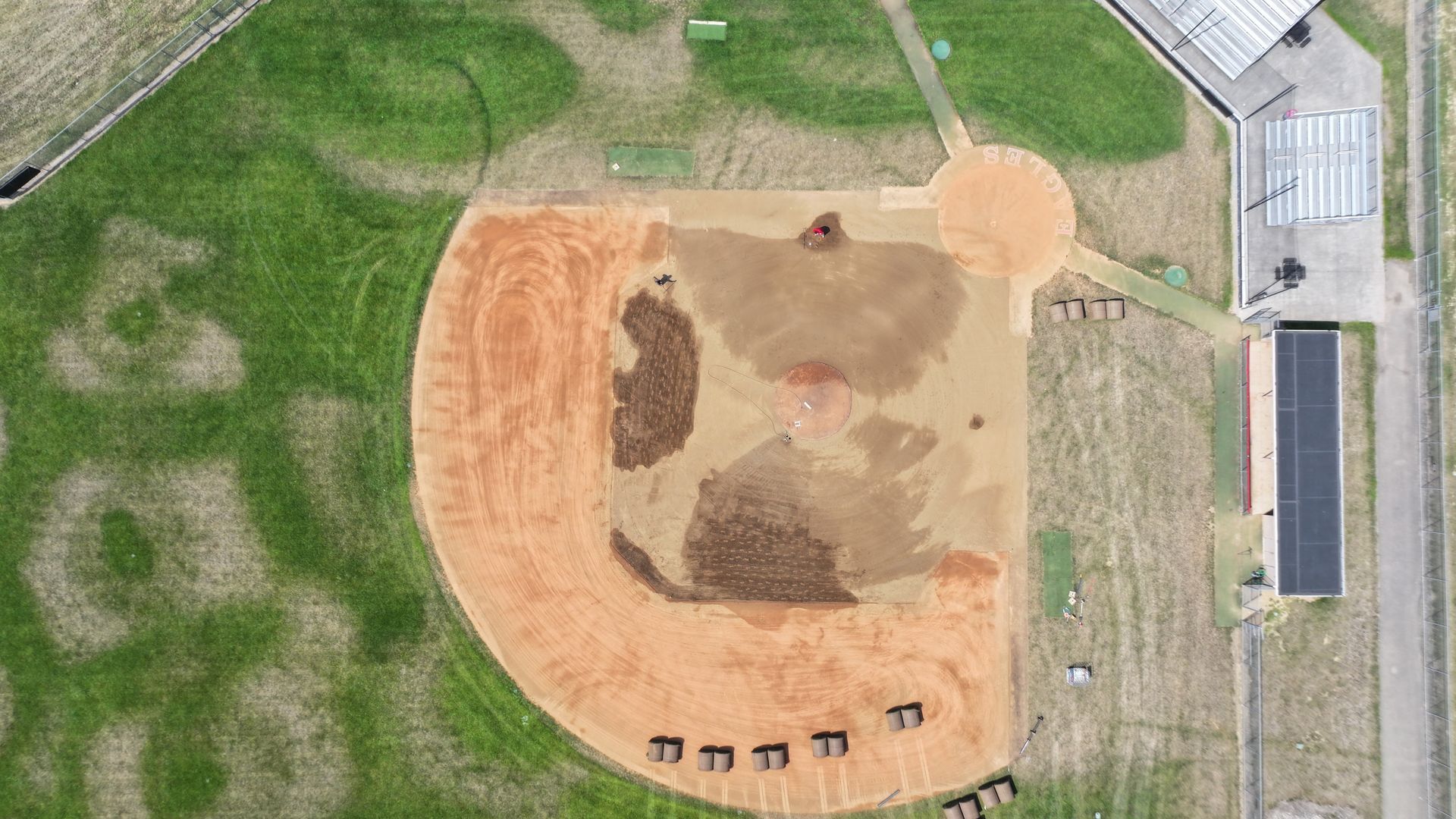 Aerial view of a baseball field with a dirt infield, green outfield, and surrounding paths and buildings