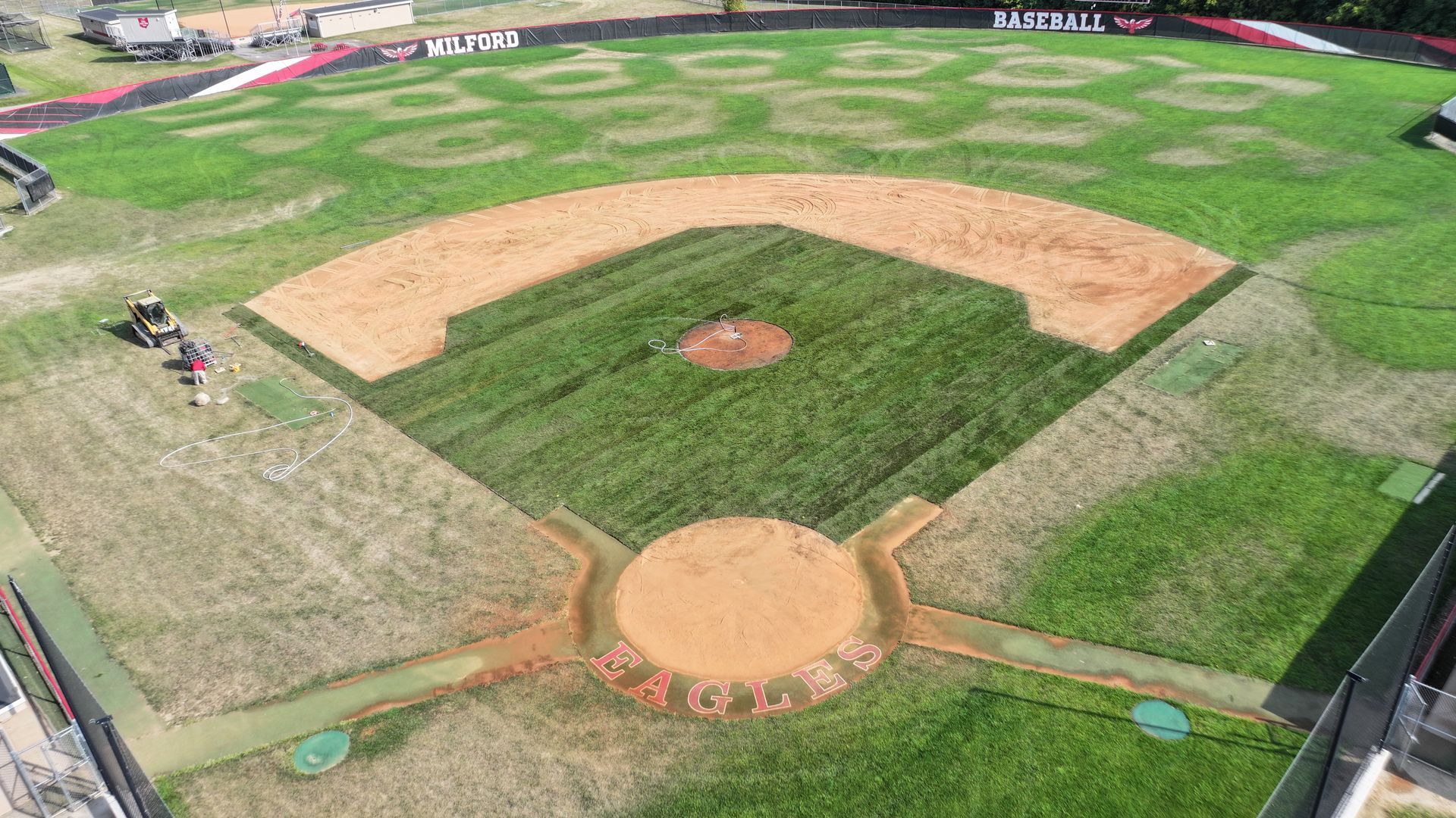 Aerial view of a baseball field with green outfield, dirt infield, and empty stands