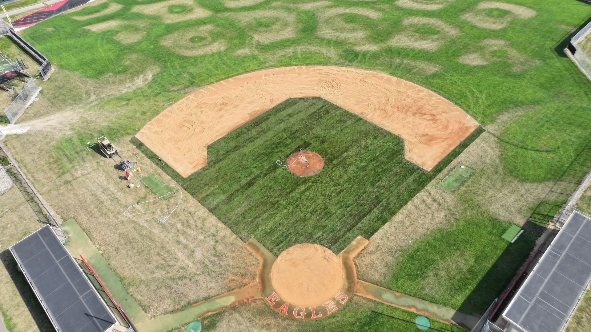 Aerial view of a baseball field with brown infield dirt, green grass, and players near the left sideline.