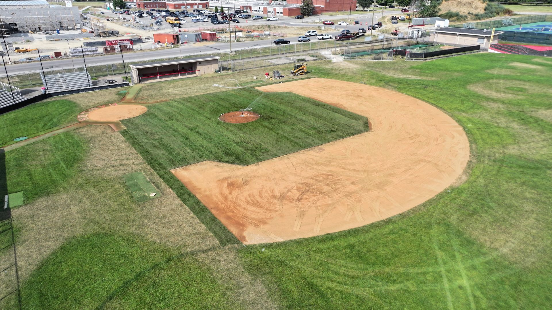 Aerial view of a baseball field with tan infield dirt and green grass beside a roadway.