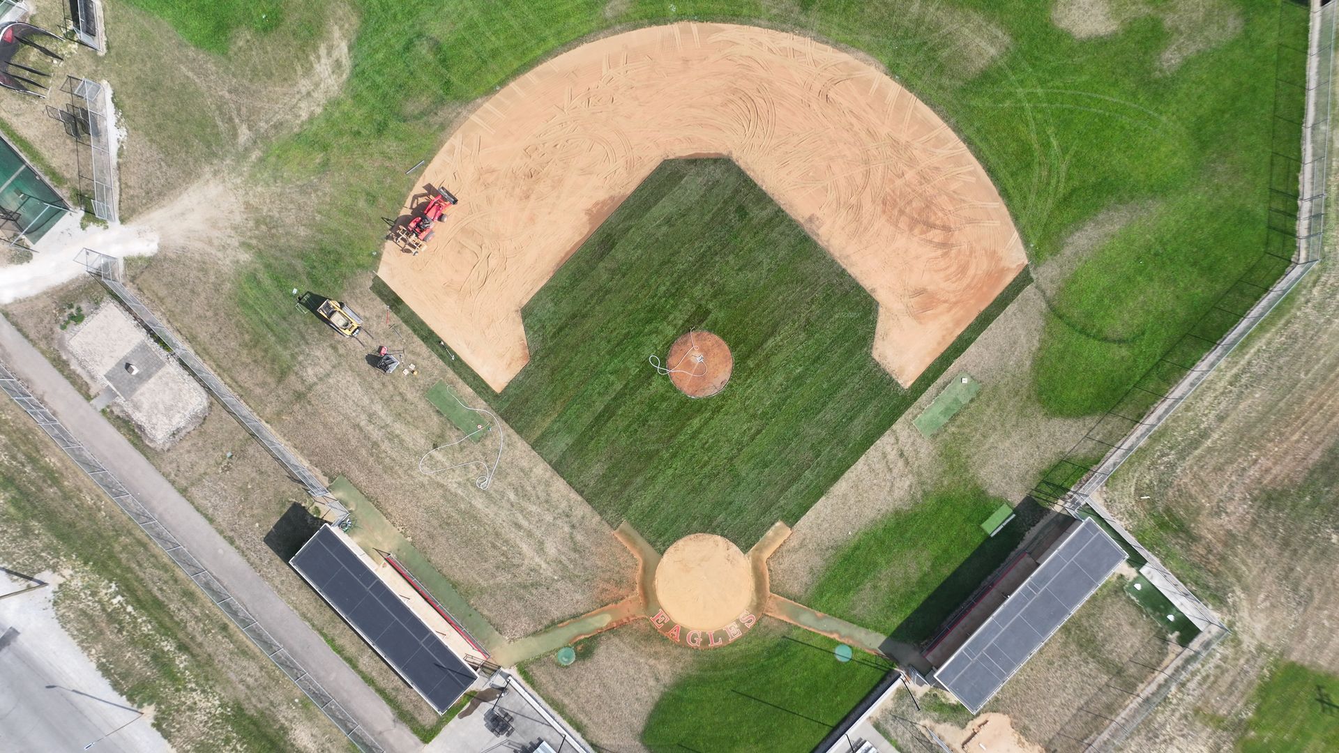 Aerial view of a baseball field with tan infield, green outfield, and surrounding paths and grass.
