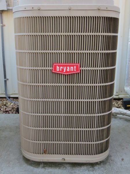 Bryant outdoor air conditioner unit with beige grille and red logo in a gravel yard