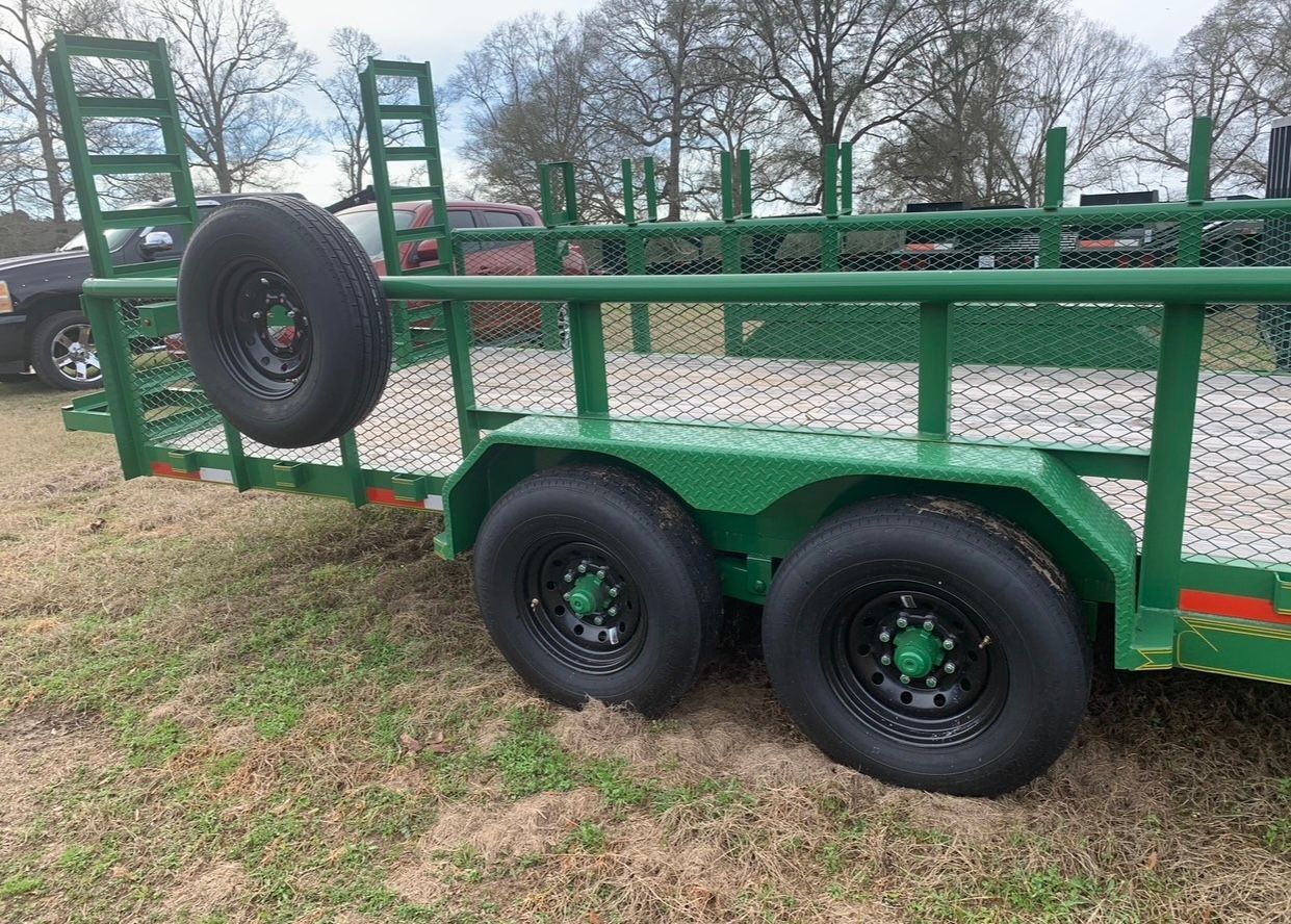 A green trailer with a spare tire on the back is parked in a grassy field.