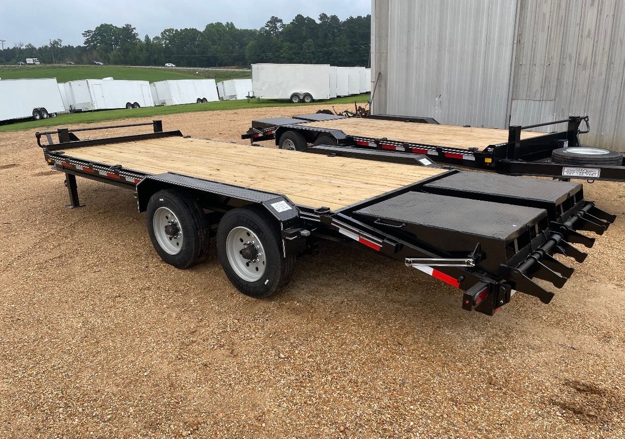 A flatbed trailer is parked in a gravel lot in front of a building.