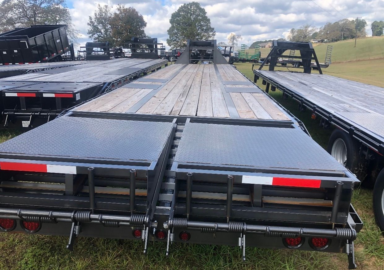 A row of flatbed trailers are parked in a grassy field.