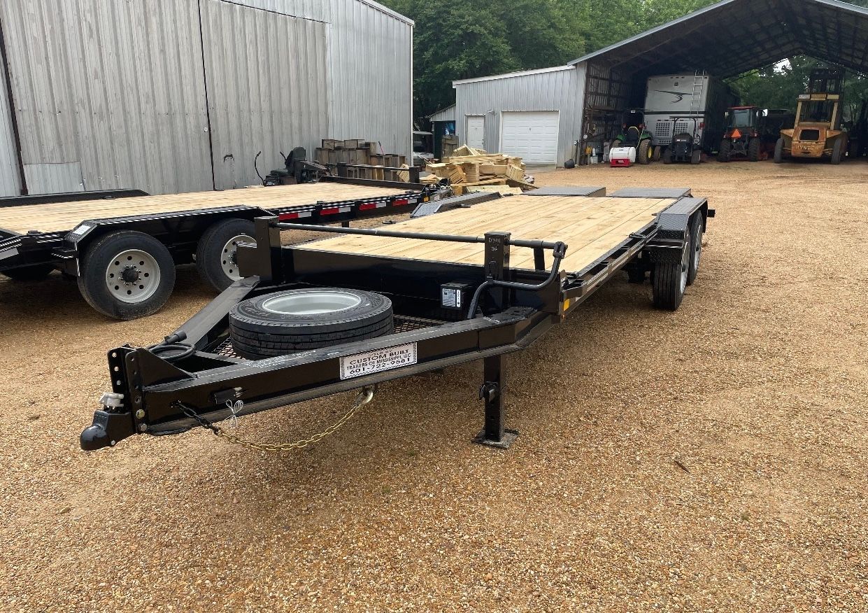 A flatbed trailer is parked in a gravel lot in front of a building.