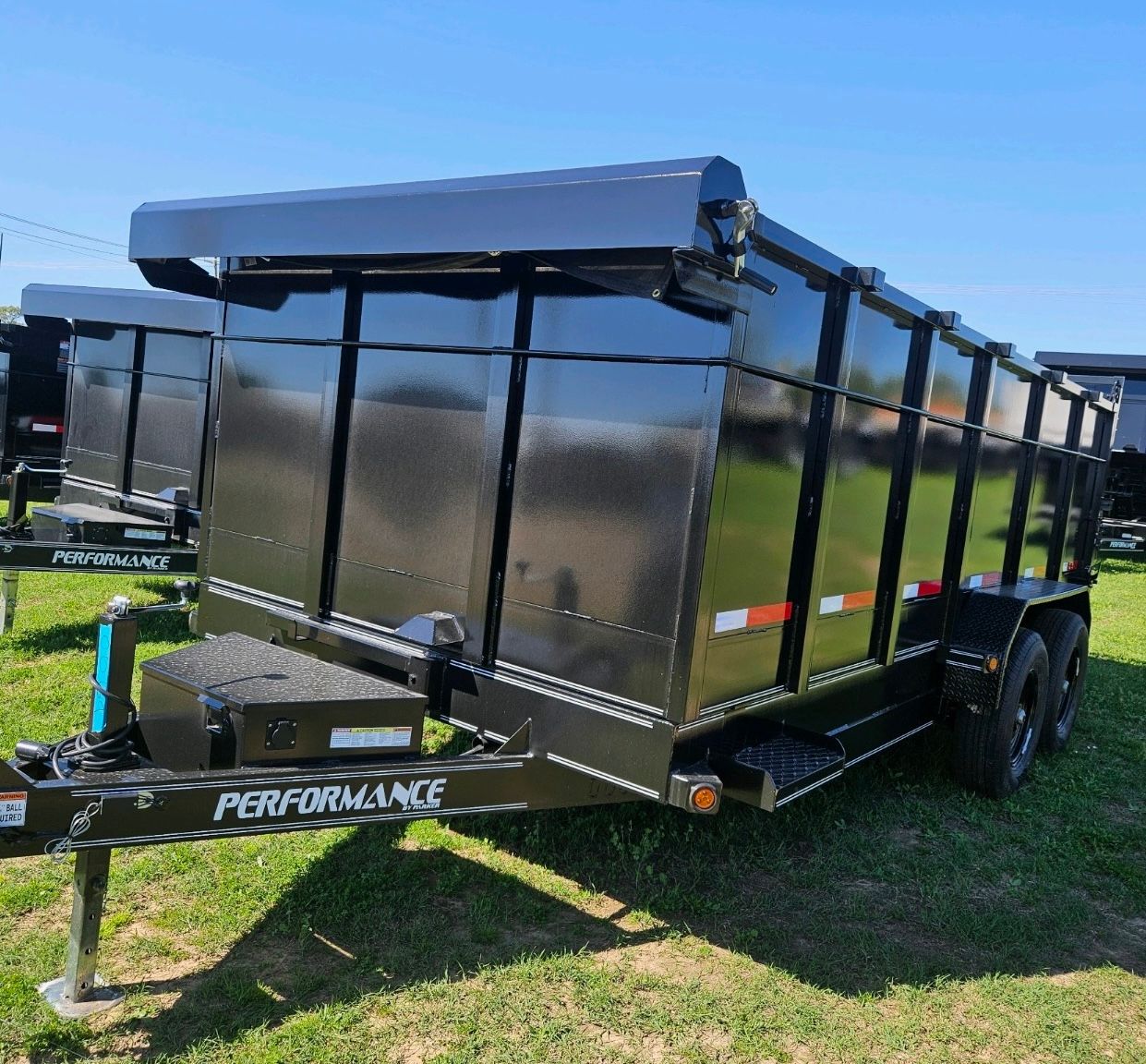 A black dump trailer is parked in a grassy field.