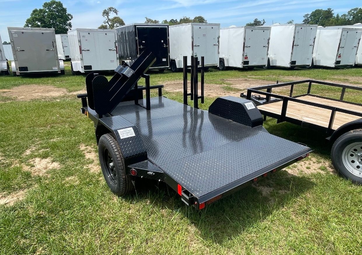A black trailer with a motorcycle on it is parked in a grassy field.