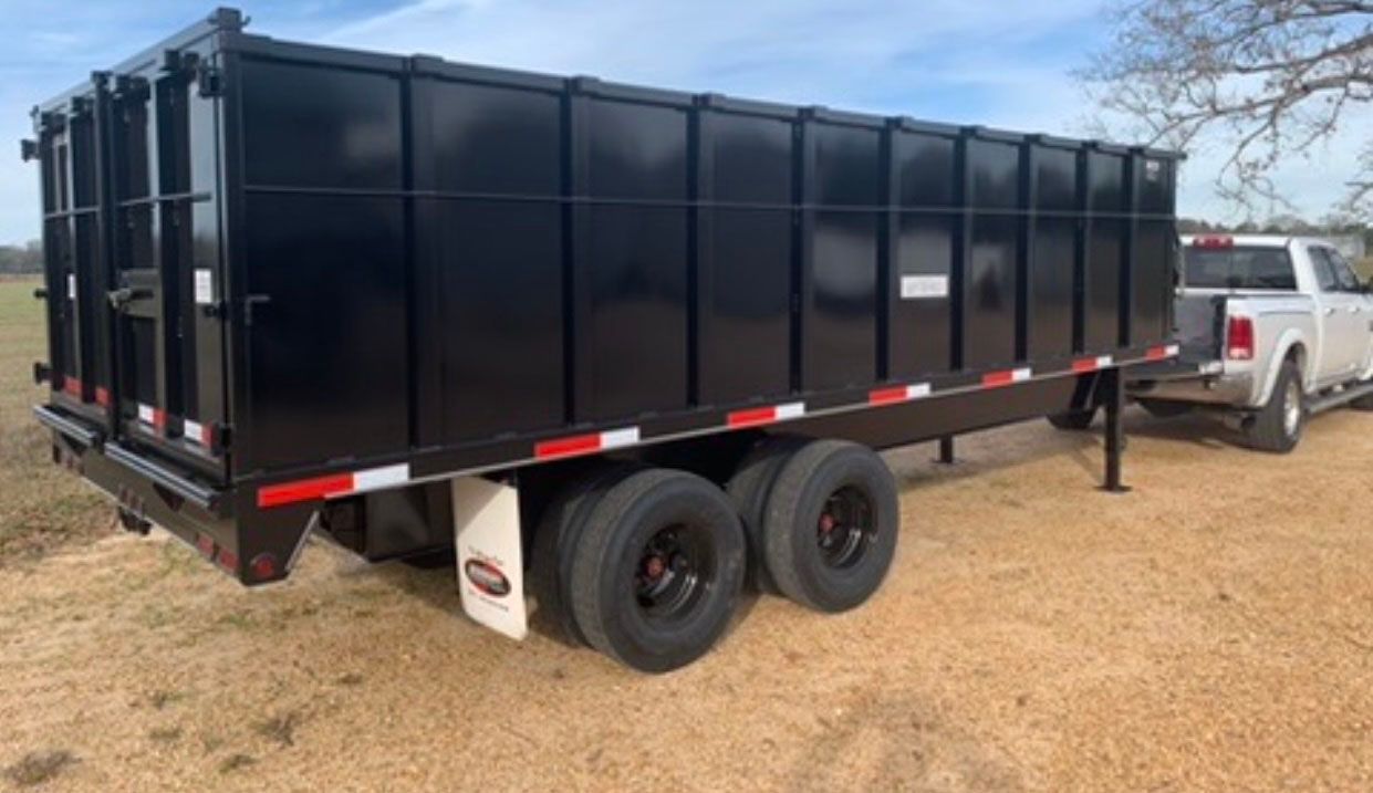 A dump trailer is parked next to a truck in a dirt field.