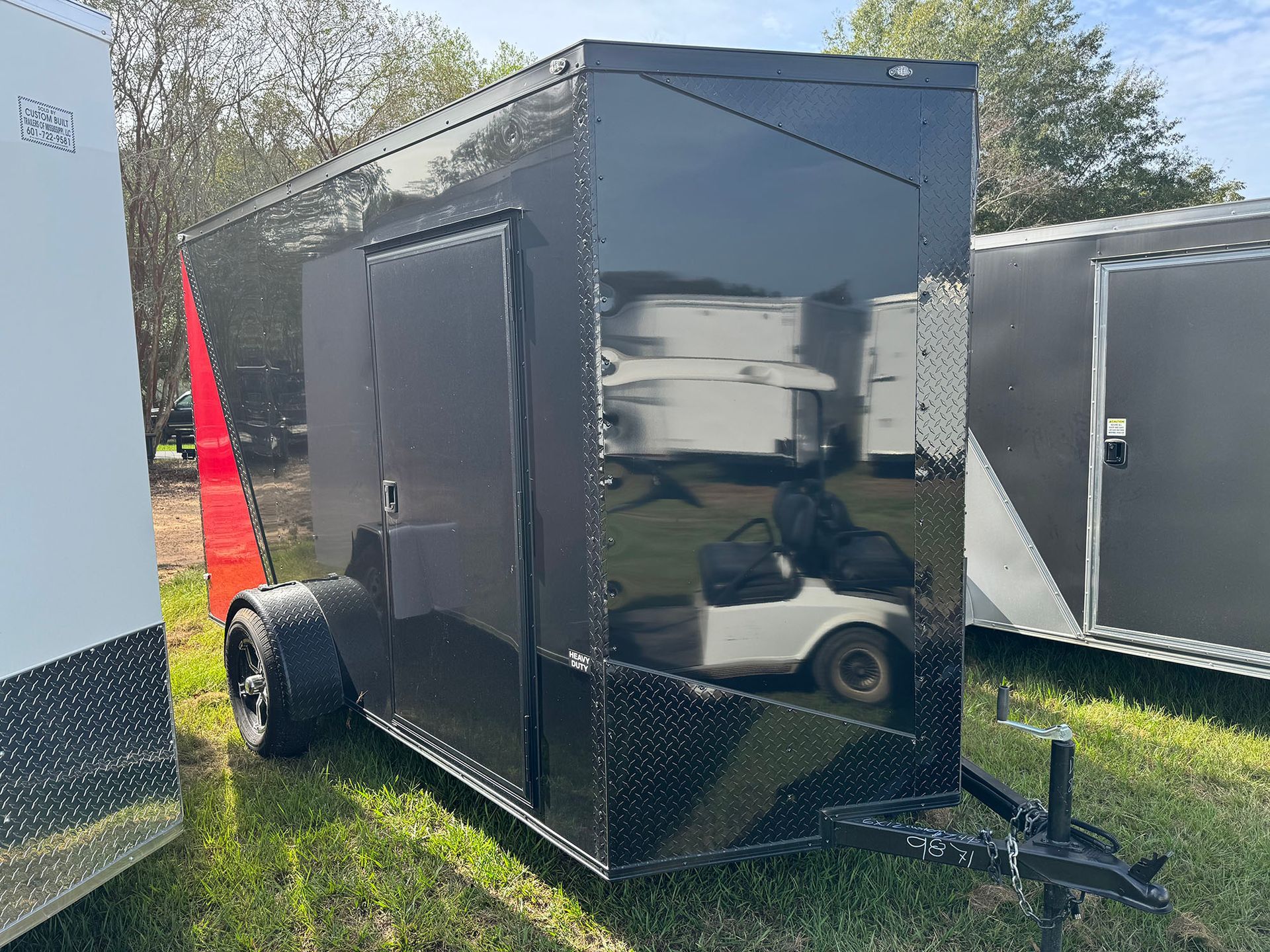 A black trailer is parked in the grass next to a golf cart.