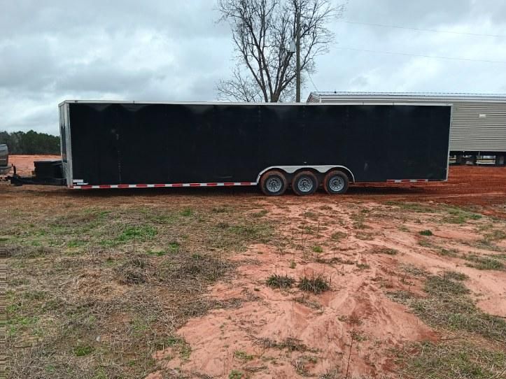 A black trailer is parked in a dirt field.