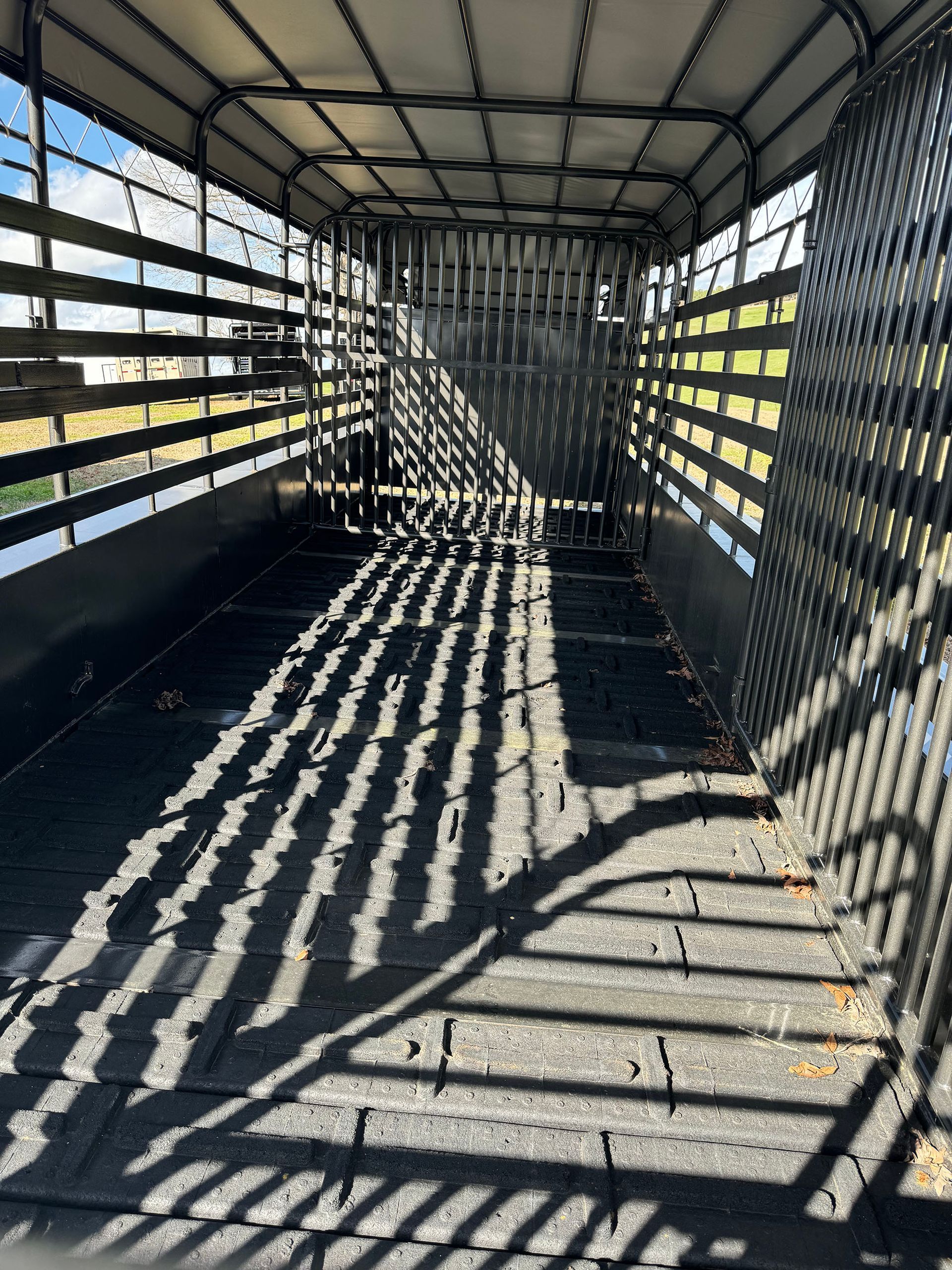The inside of a truck with a fence and shadows on the floor.