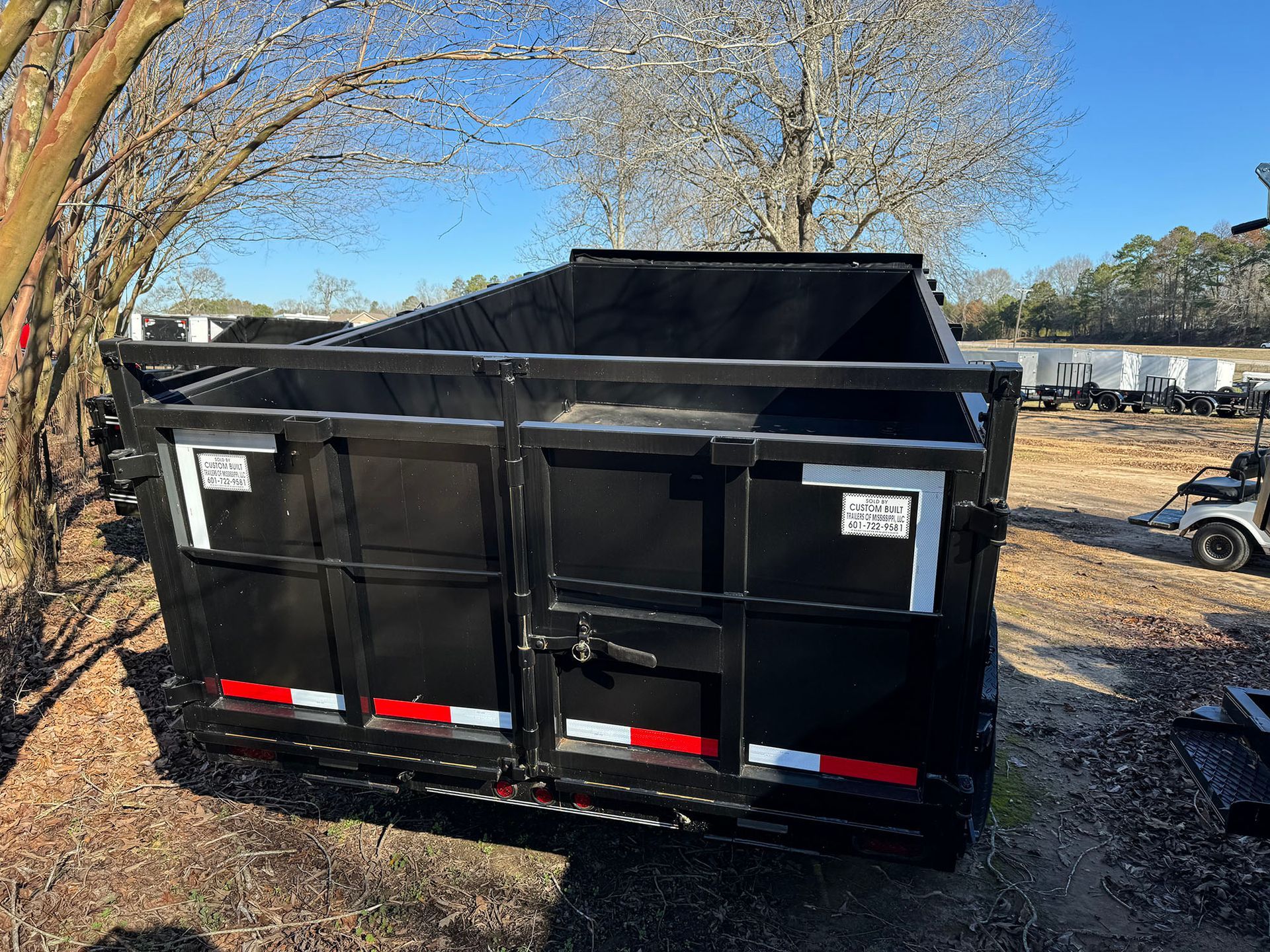 A dumpster is parked in a field next to a tree.