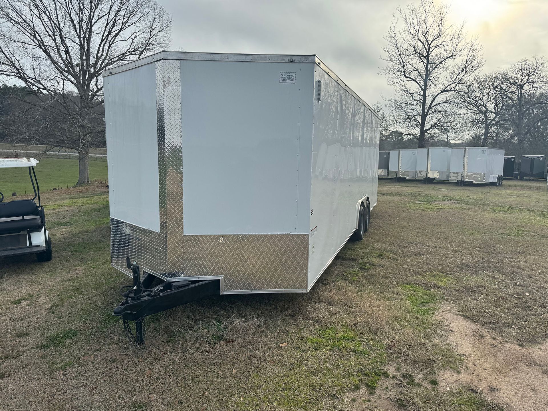 A white trailer is parked in a grassy field next to a golf cart.