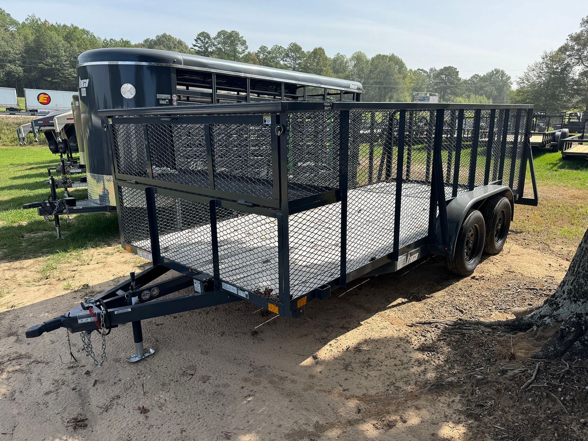A trailer is parked in a dirt field next to a tree.