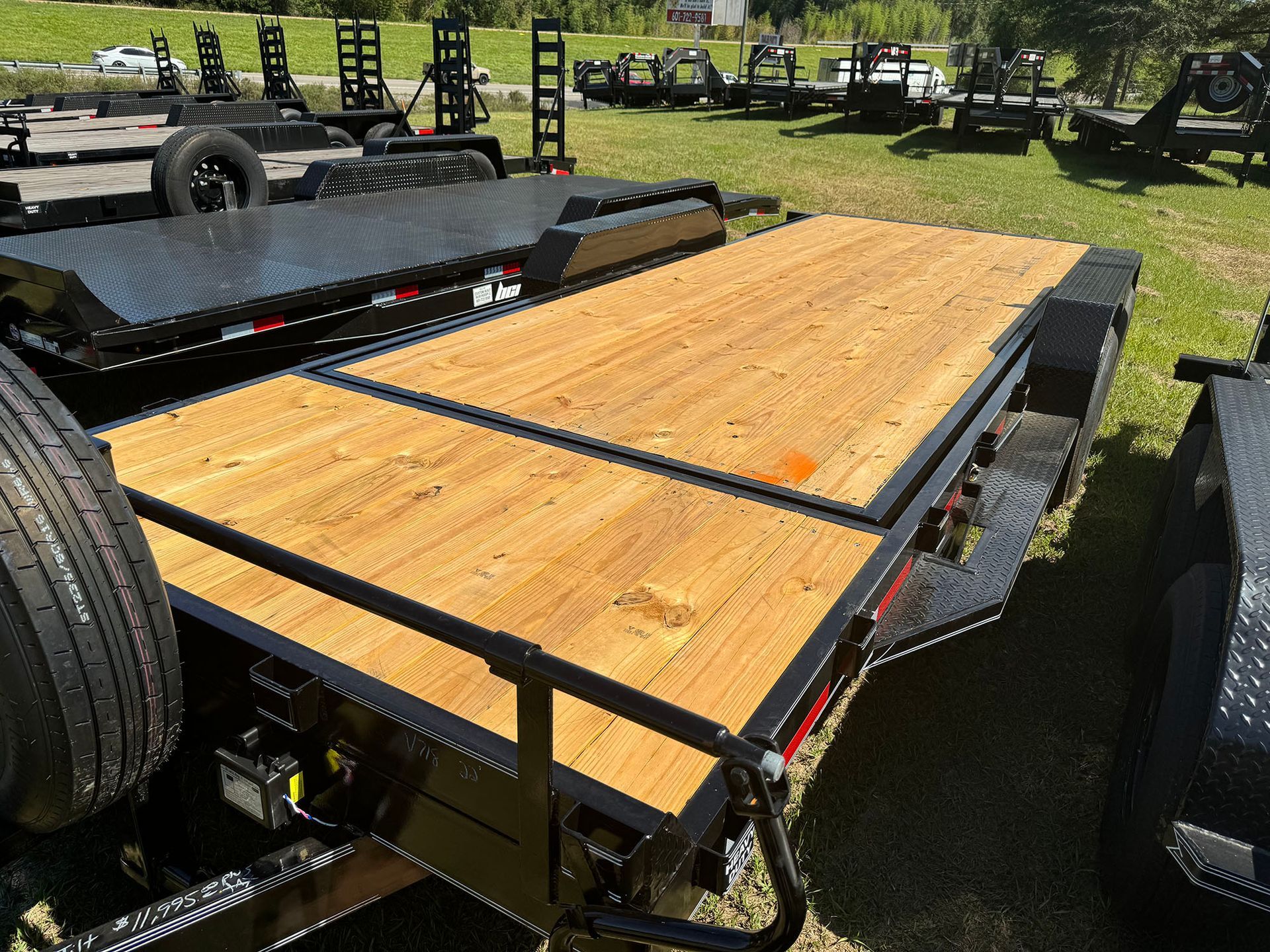 A trailer with a wooden deck is parked in a grassy field.