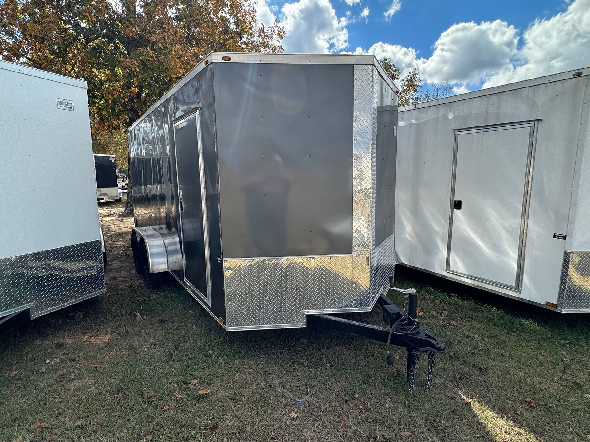 A trailer is parked in a grassy field next to a white trailer.