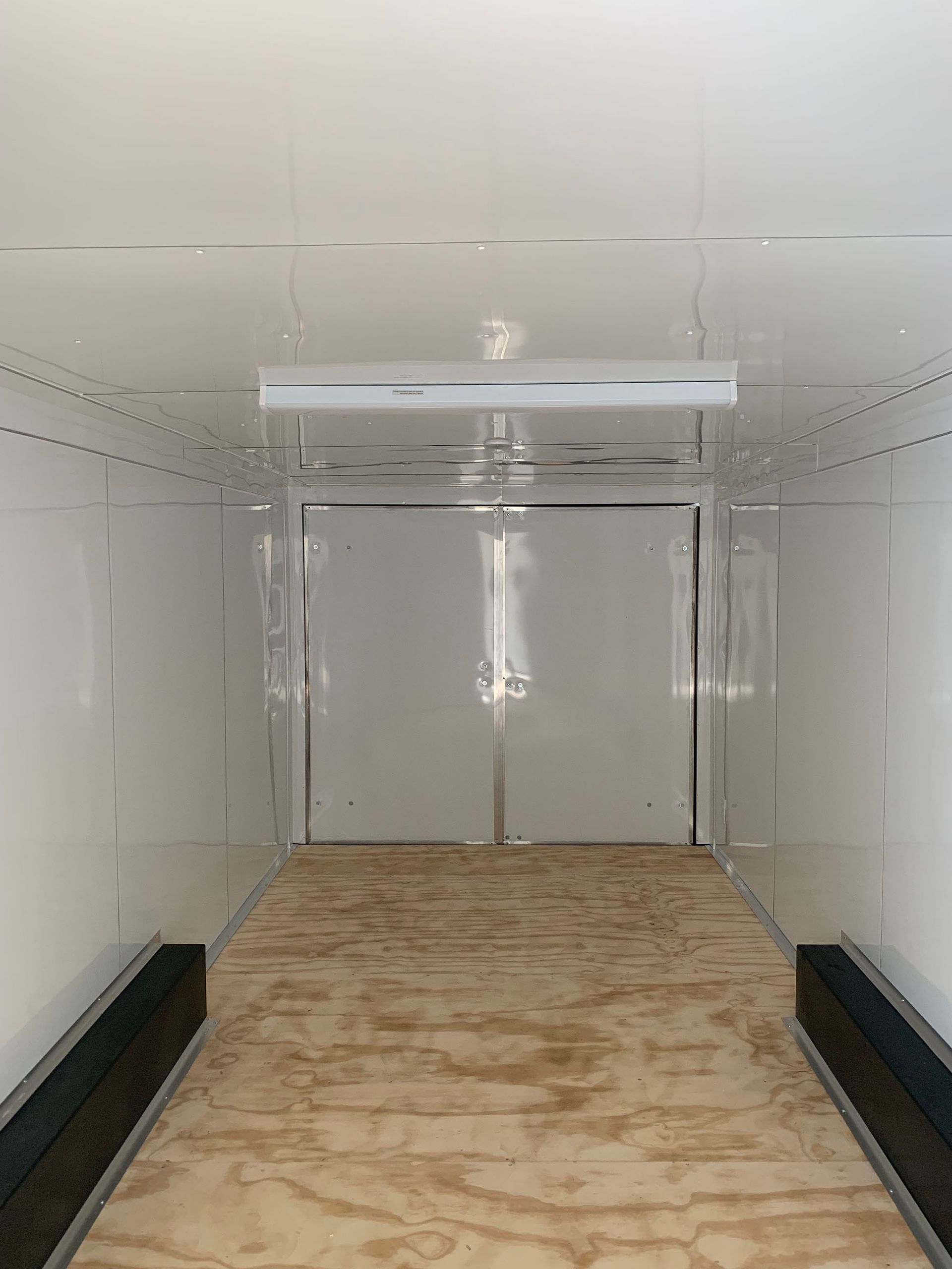 The inside of a trailer with a wooden floor and white walls.