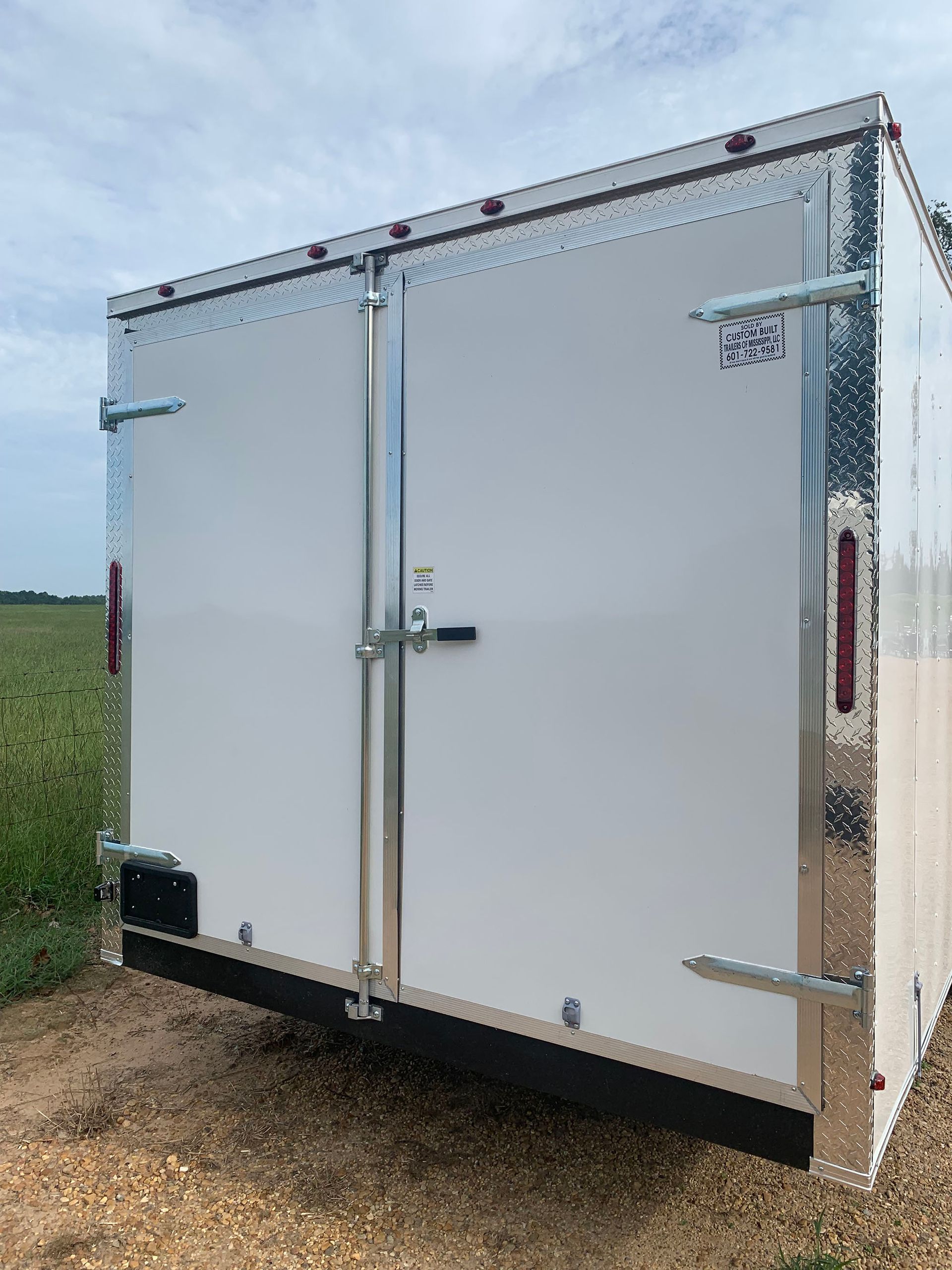 A white trailer is parked in the dirt in a field.