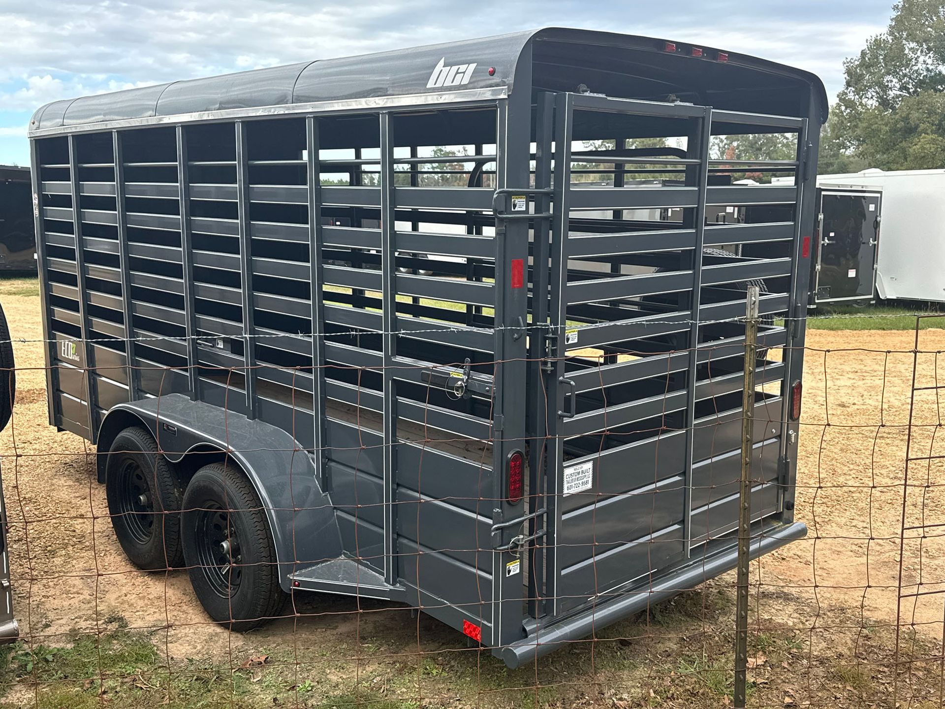 A horse trailer is parked in a field next to a fence.